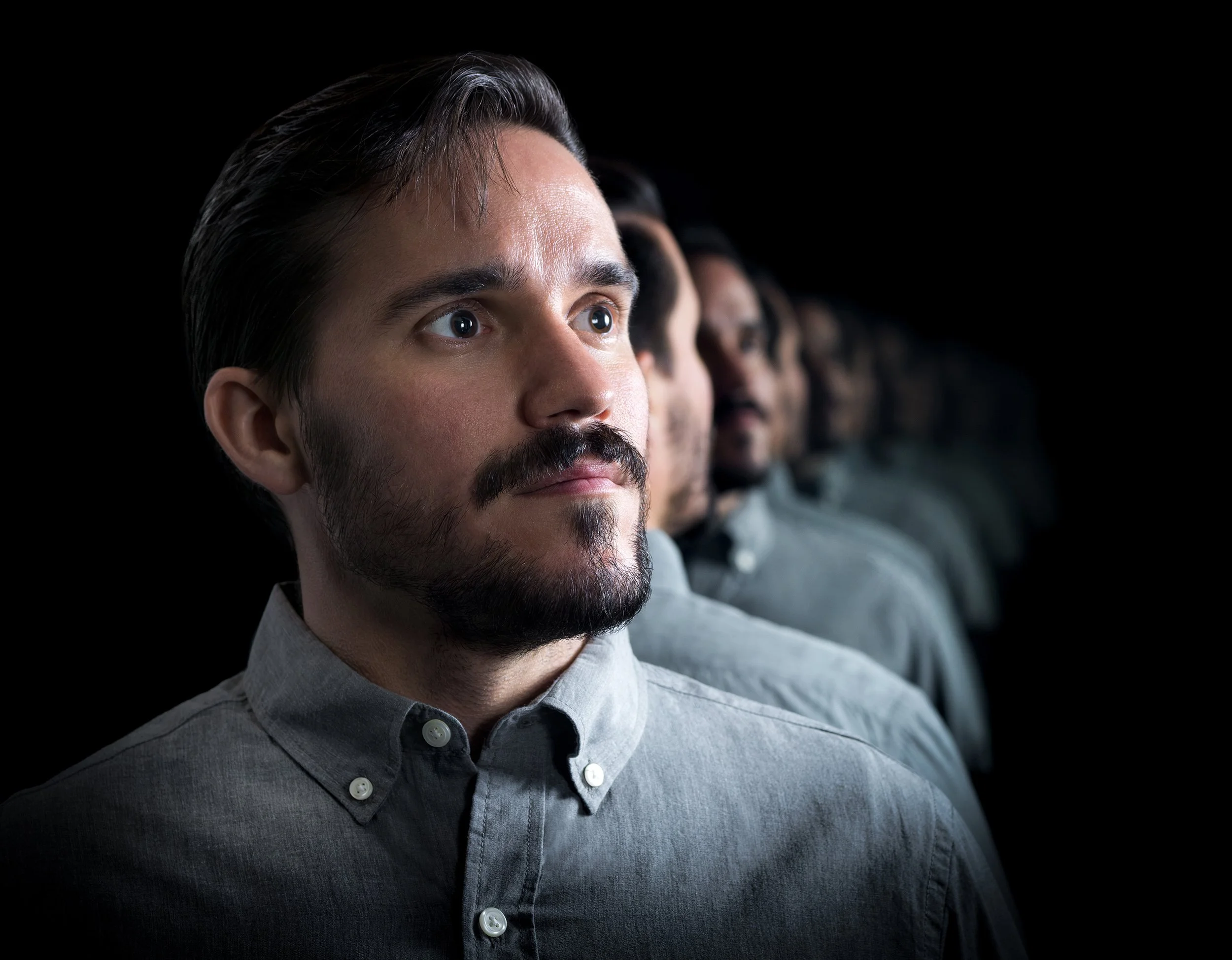 Line of men in formal shirts seated in a row, looking ahead with serious expressions.