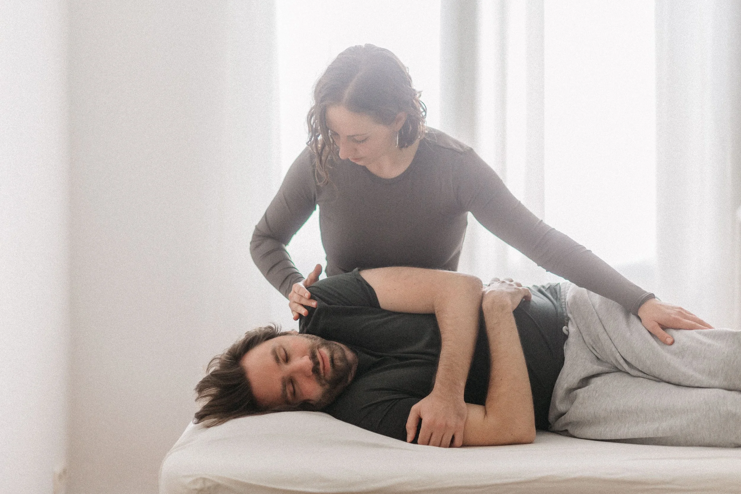 Eine Frau gibt einem liegenden Mann eine Pantarei-Sitzung. Der Mann liegt auf einer Massageliege in einem hellen Raum. Beide wirken entspannt.