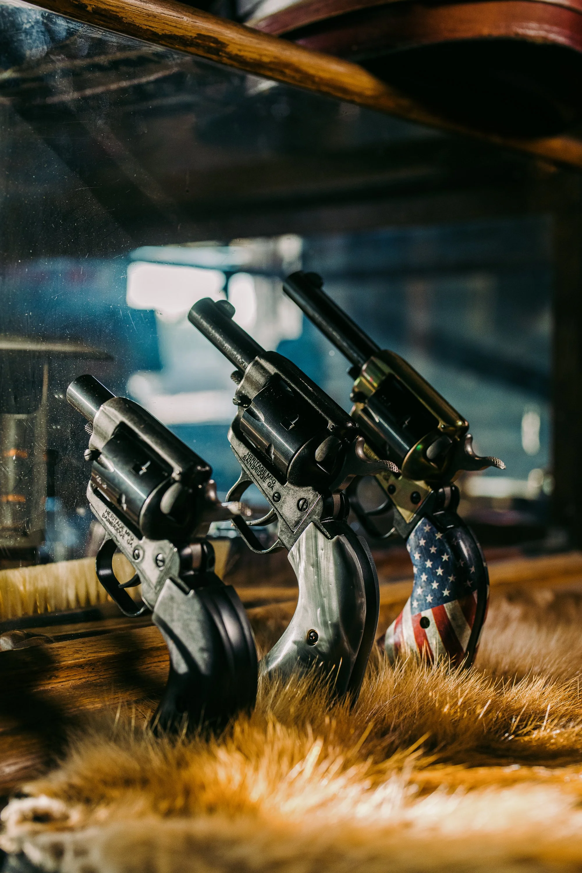 Three antique revolvers with distinctive handles displayed in a wooden case; one handle features an American flag design.