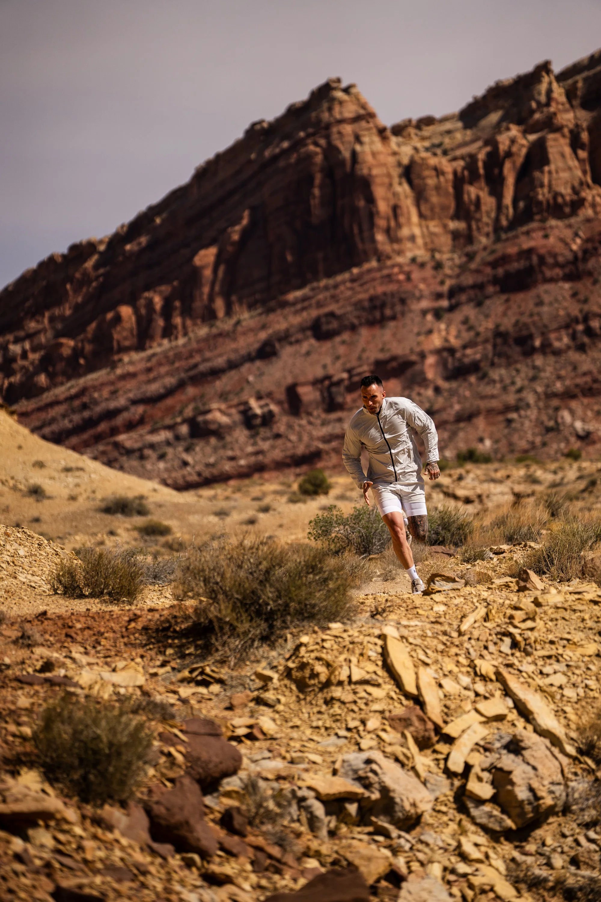 Man running on rocky desert trail in front of large rugged cliffs.