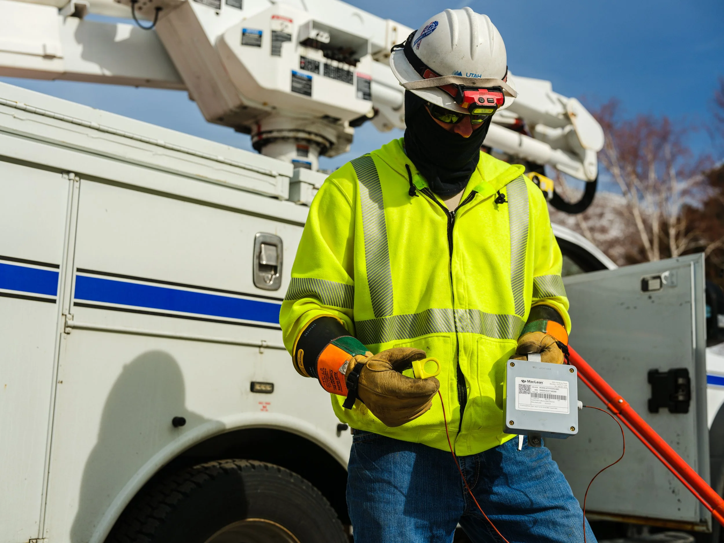 Utility worker in safety gear and helmet standing by service truck, holding equipment on a clear day.