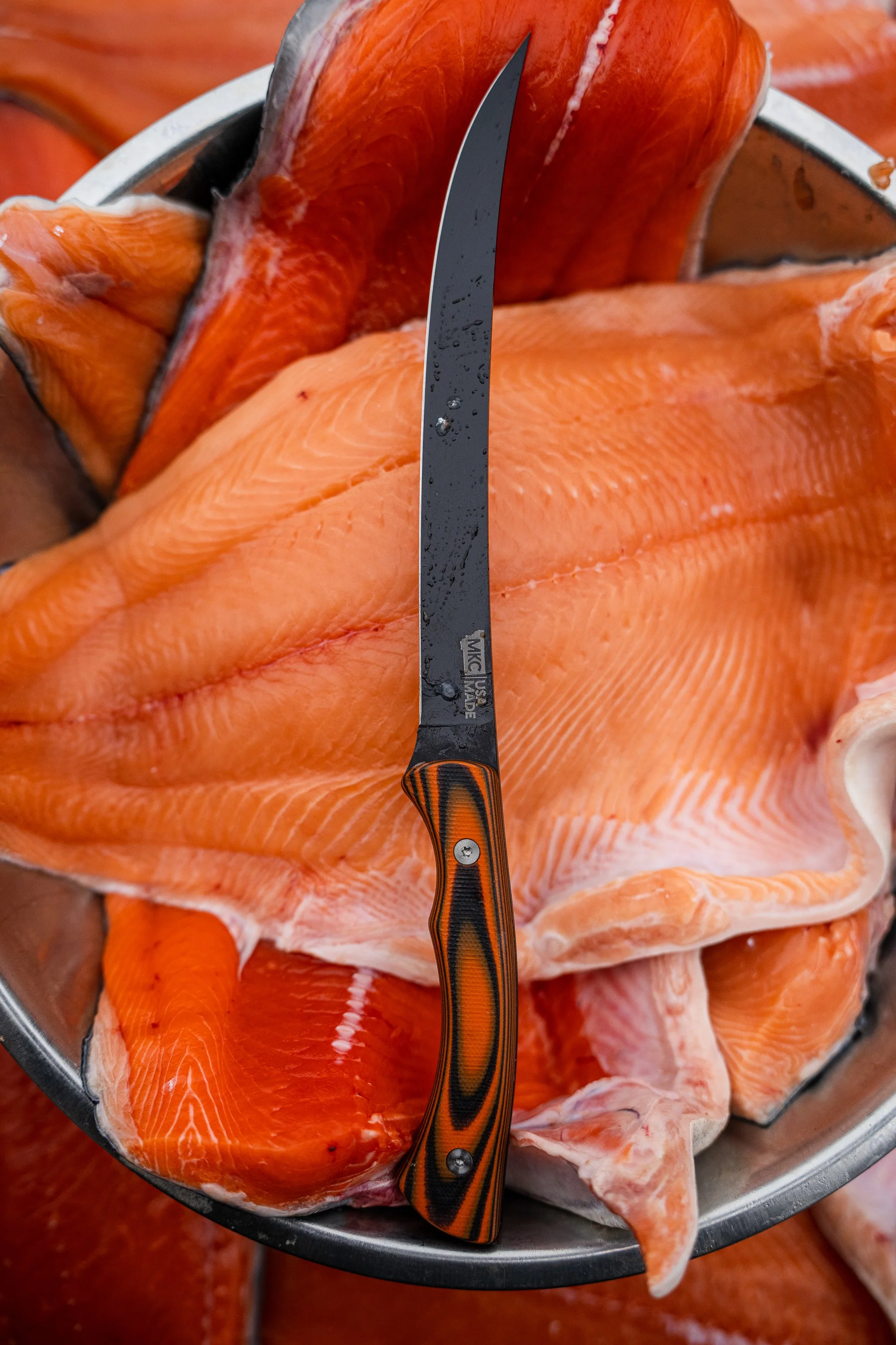 Fillet knife resting on salmon fillets in a metal bowl.