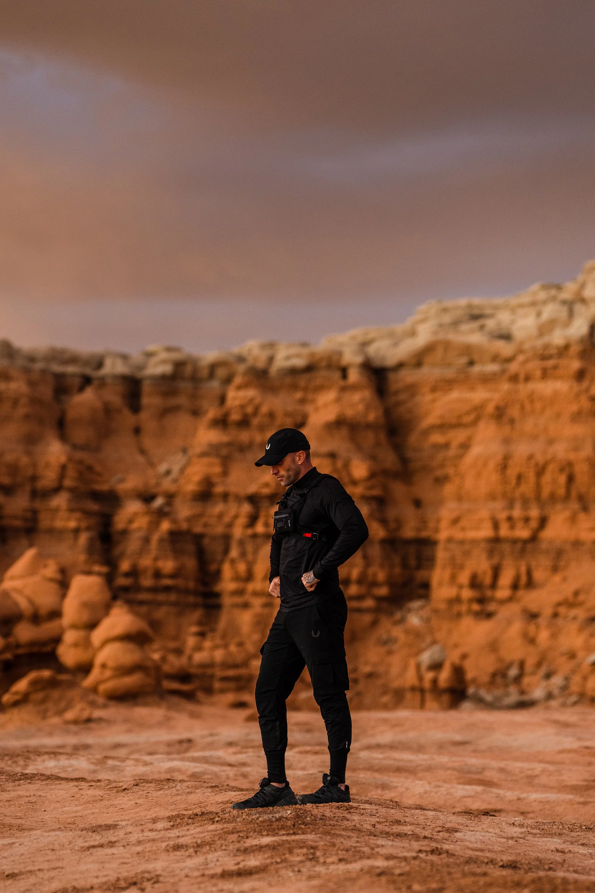 Person in black attire standing in a desert landscape with orange rock formations at sunset.