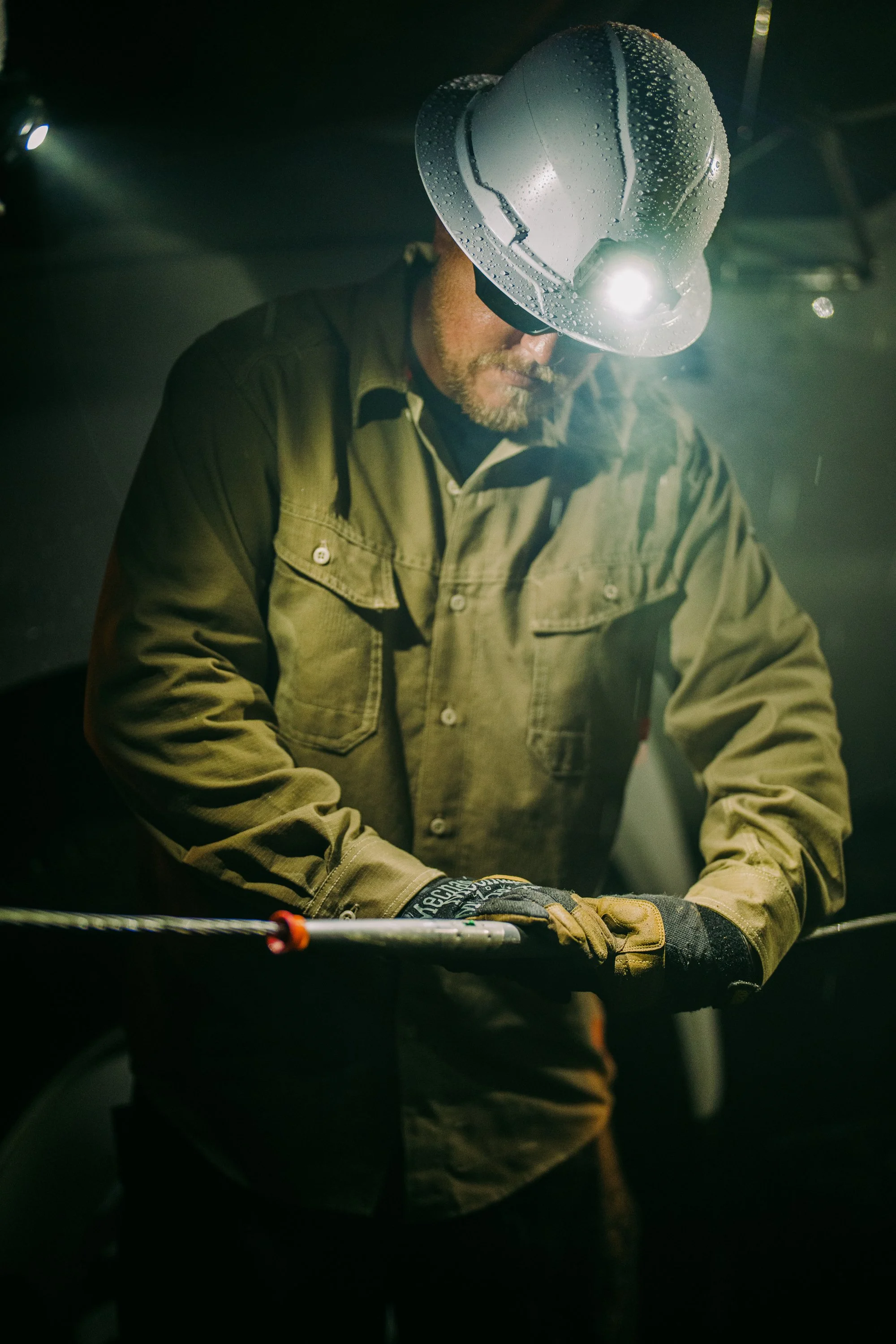 Worker adjusting cable in dim lighting with headlamp and safety gear