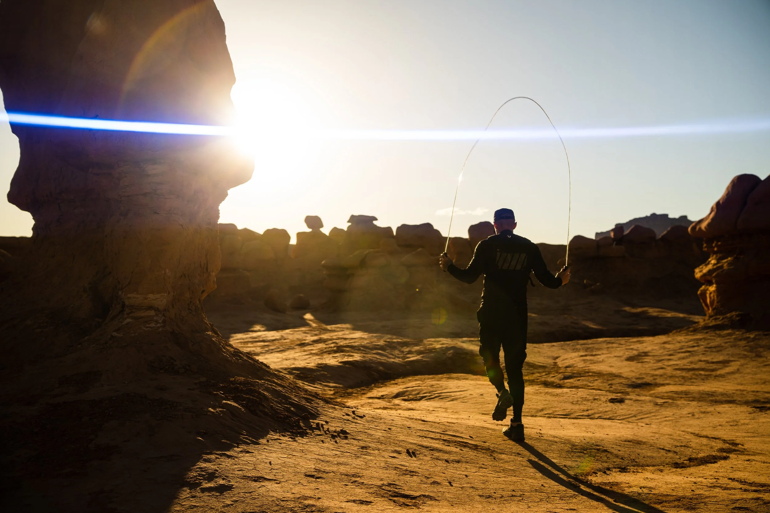 Person jump roping in a desert landscape at sunset, with sunlight creating lens flare.