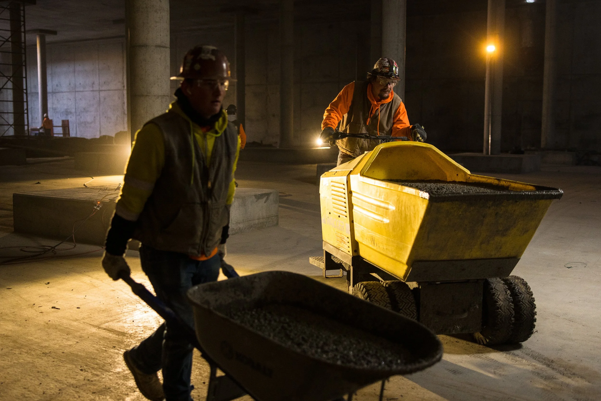 Construction workers operating machinery in a dimly lit building site.