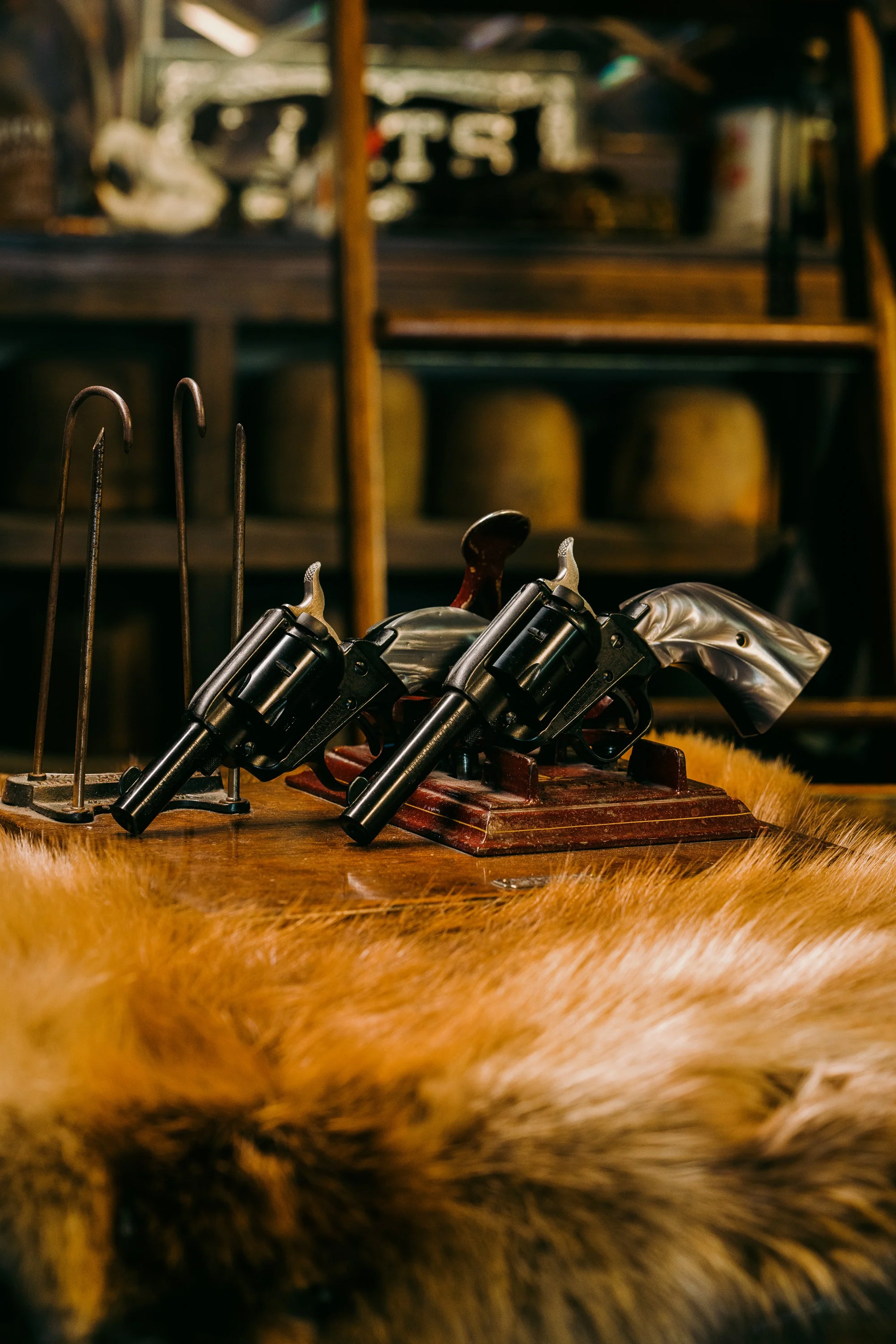 Two vintage revolvers with pearl grips displayed on a wooden stand, against a rustic background.