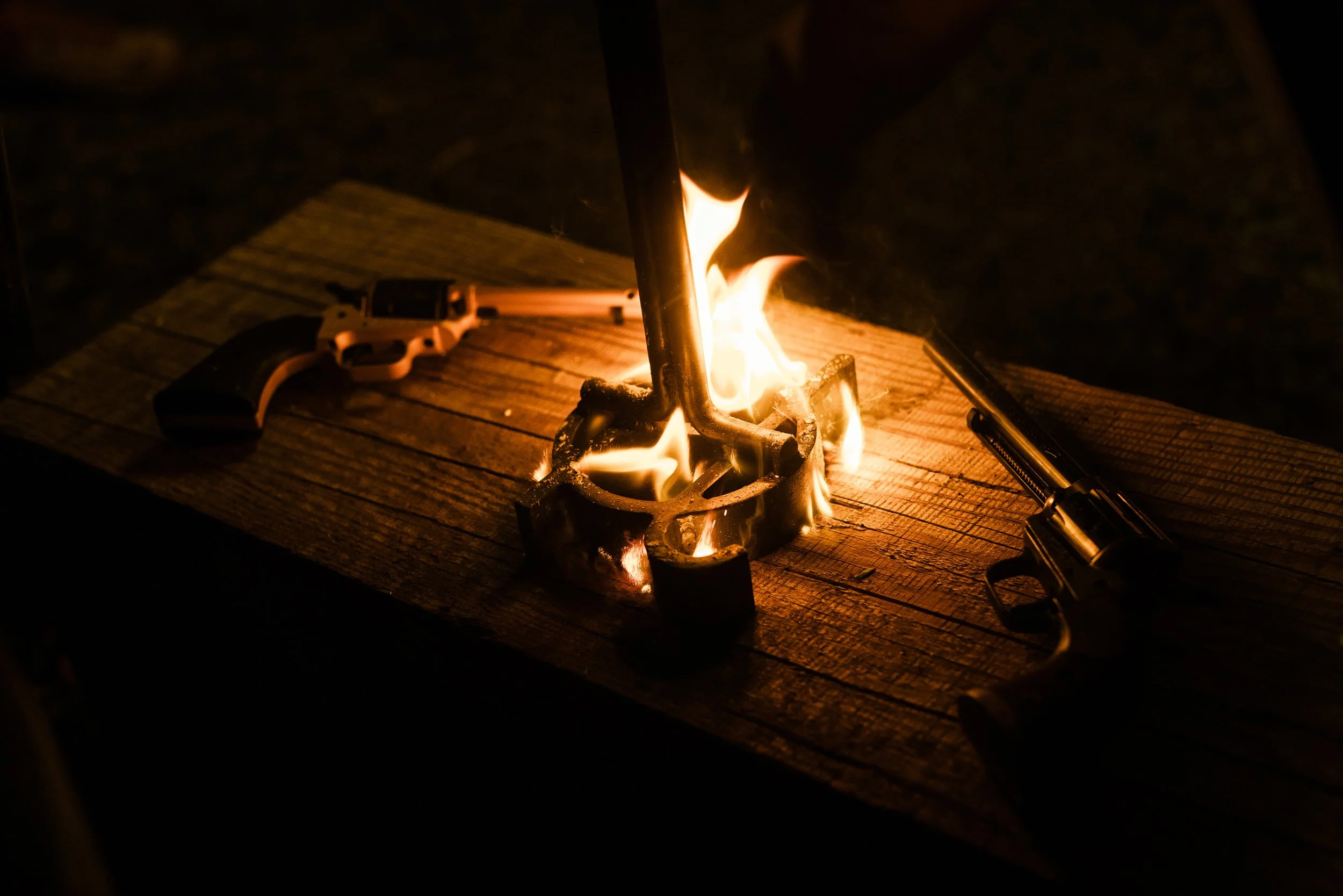 Two revolvers on a wooden table with a campfire in the center