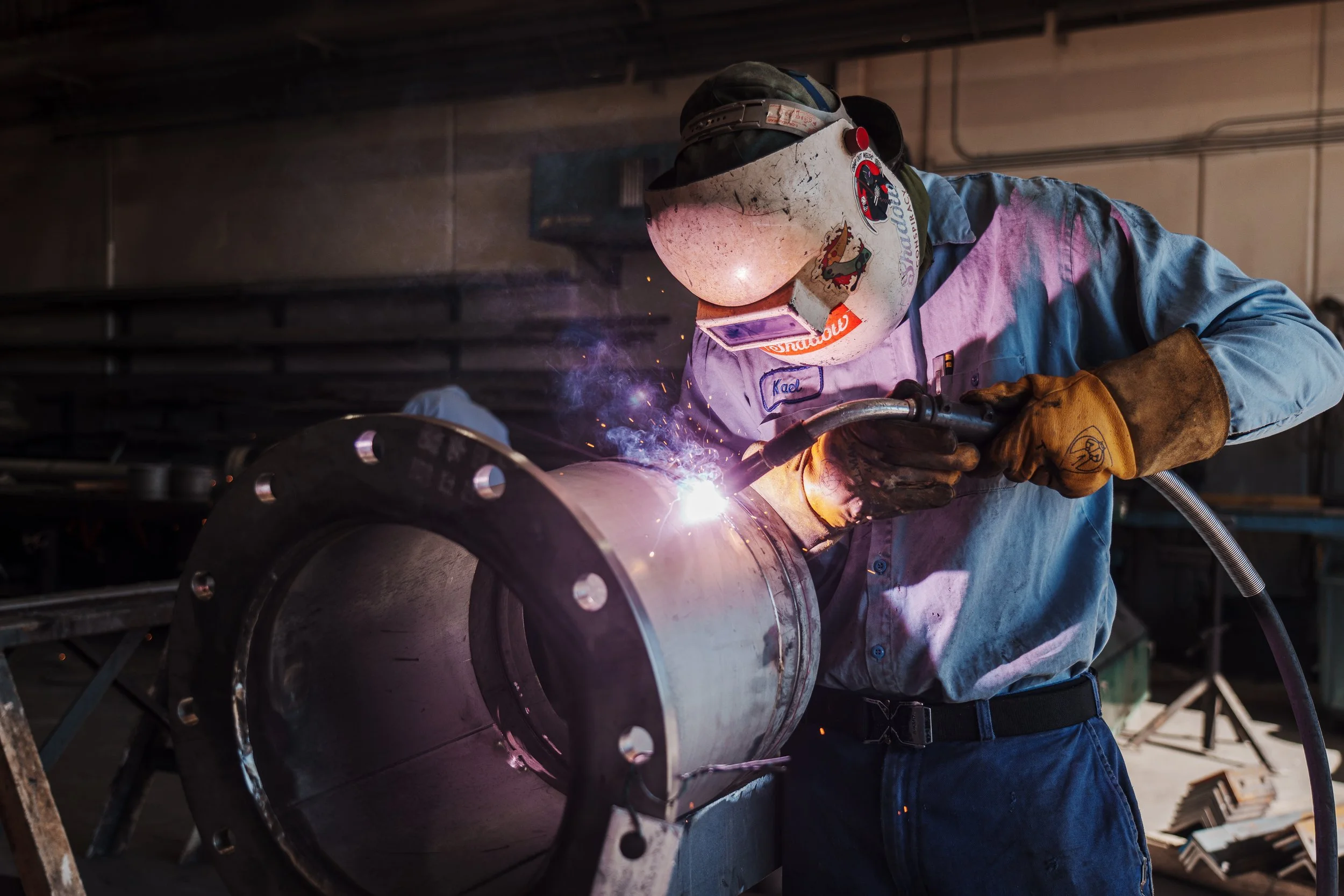 A welder in protective gear welding a metal pipe in a workshop.