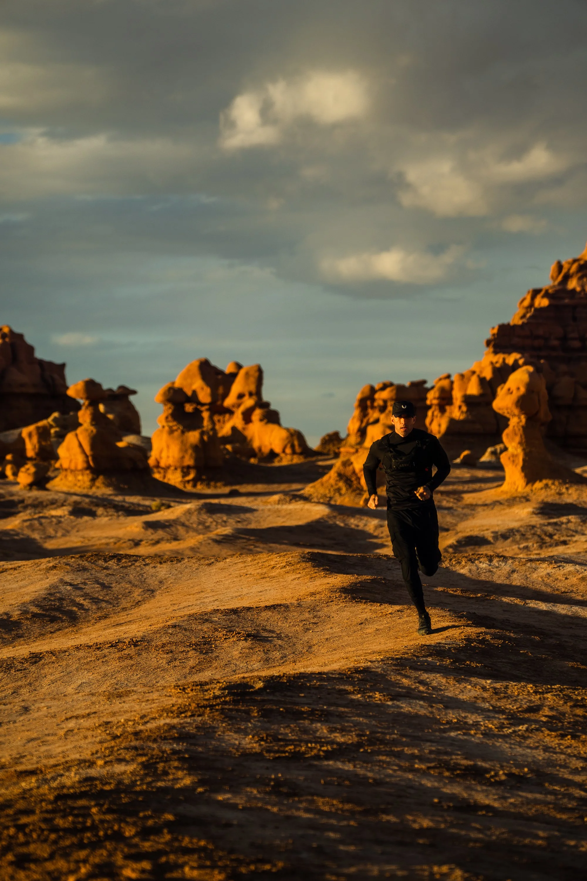 Person running in a desert landscape with eroded rock formations under a cloudy sky.