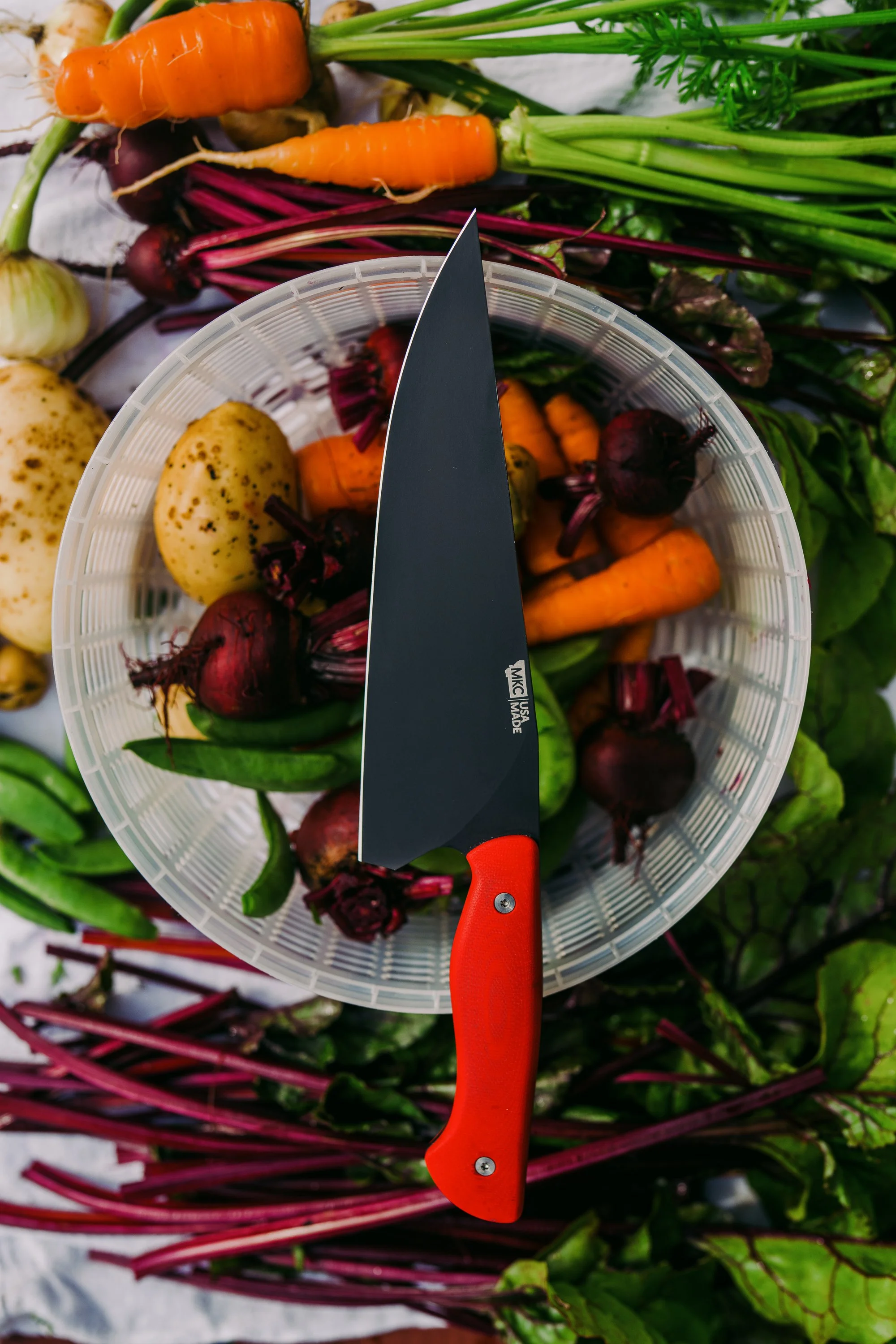 Assorted fresh vegetables including carrots, potatoes, beets, and snap peas around a knife with a red handle.