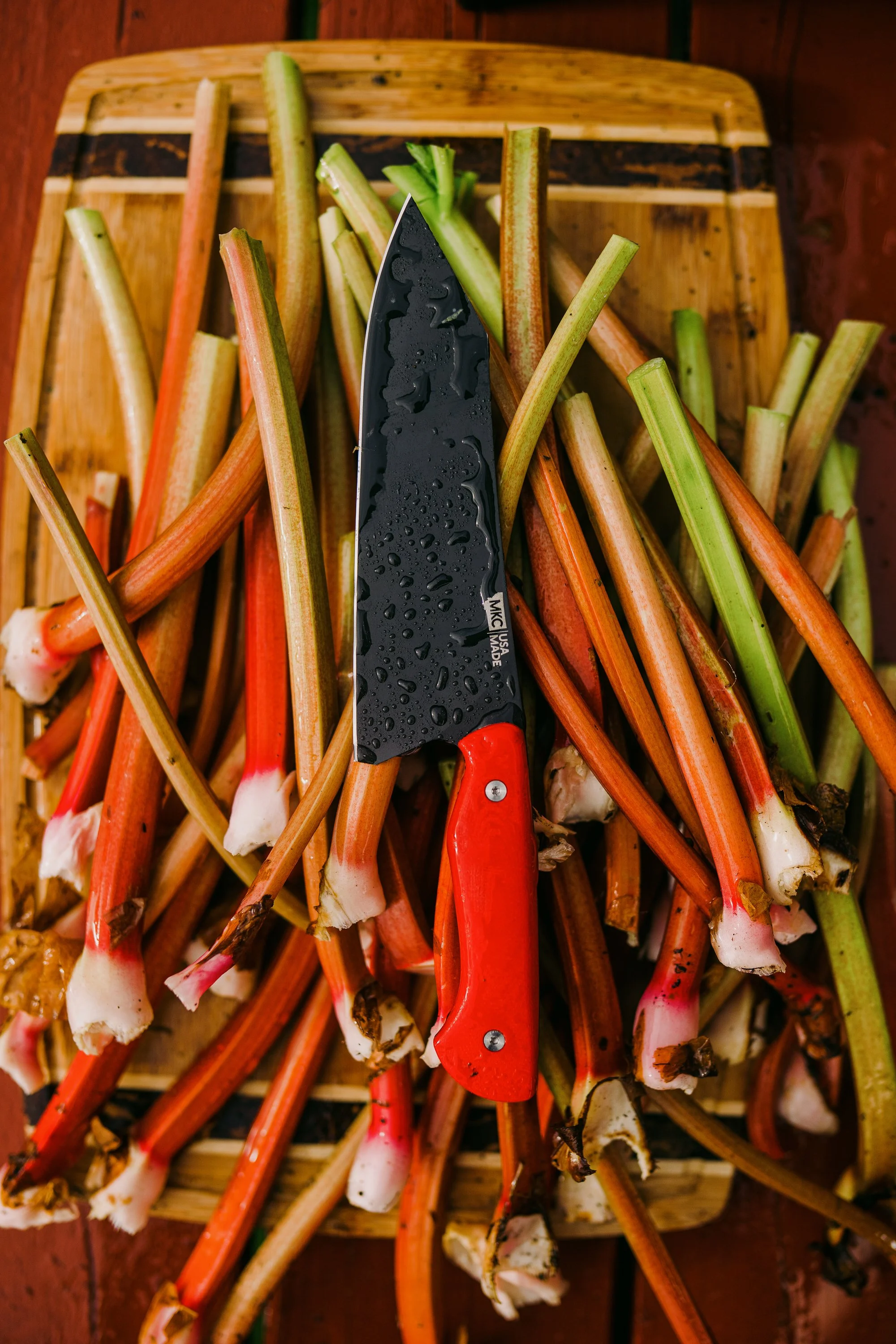 Chopping board with fresh rhubarb stalks and a black and red kitchen knife
