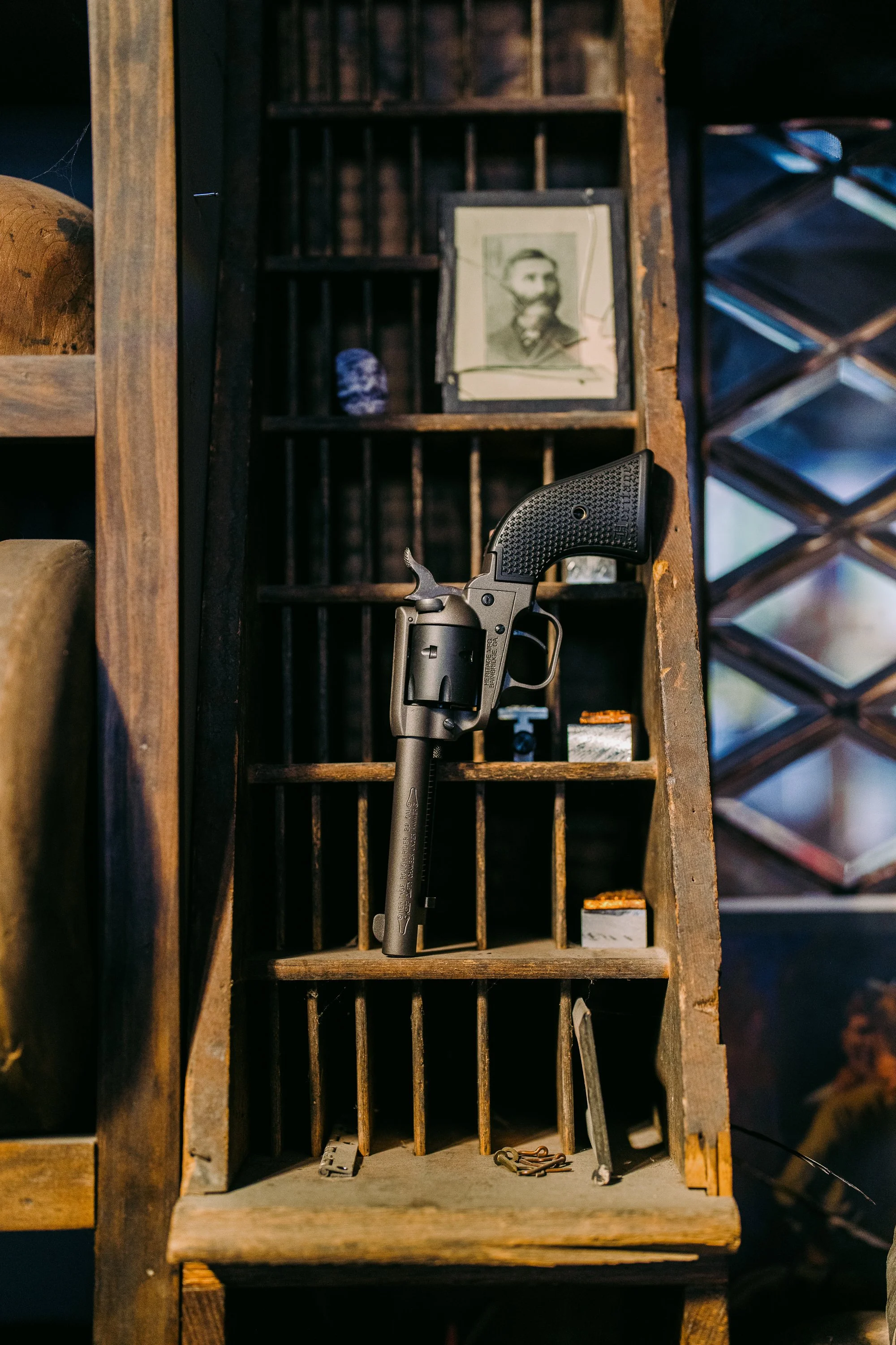 Old wooden shelf with a revolver, vintage photograph, and small items such as a thimble and trinkets.
