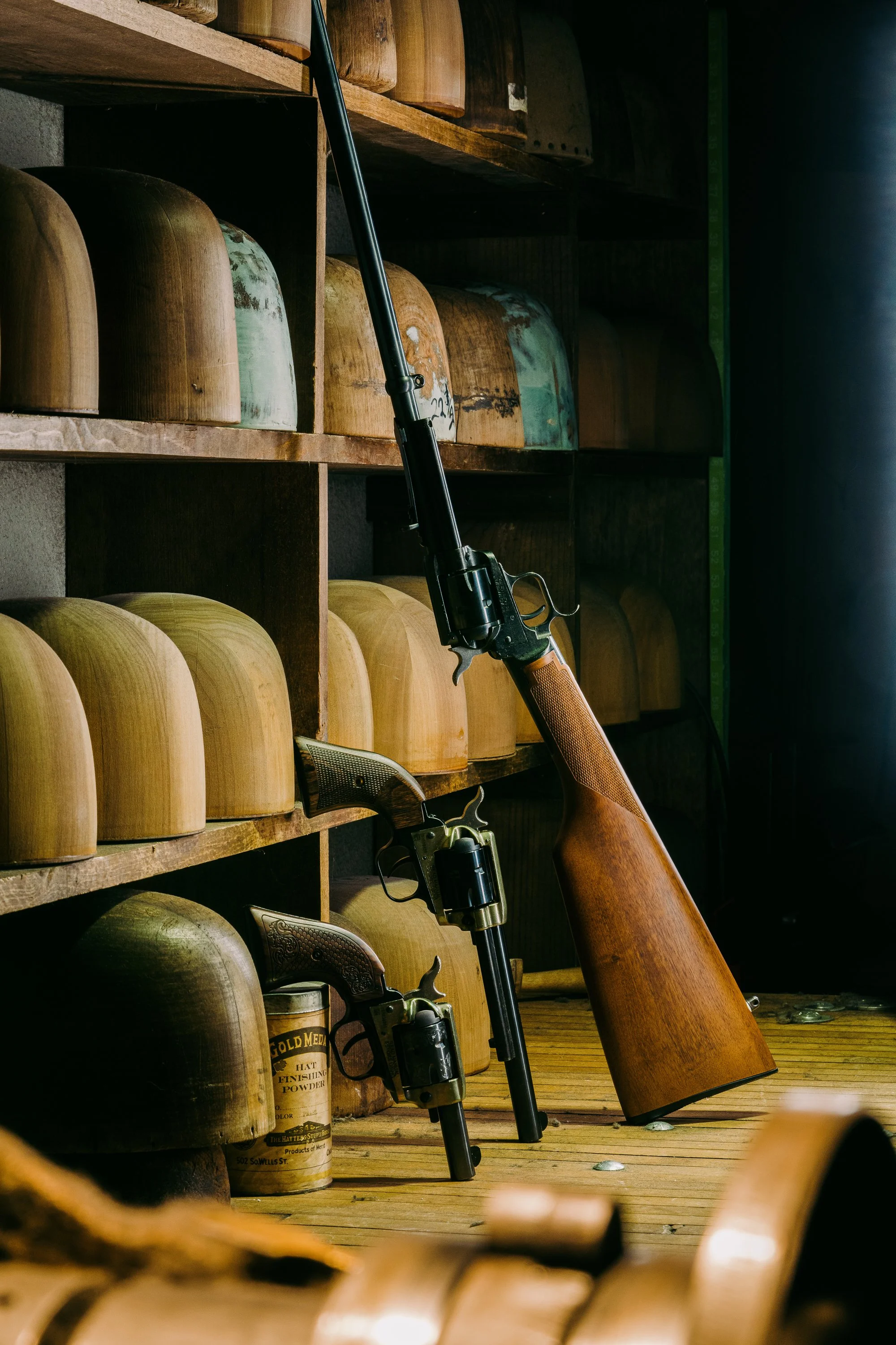Two vintage firearms, a rifle and a revolver, displayed on wooden shelves with wooden hat molds.