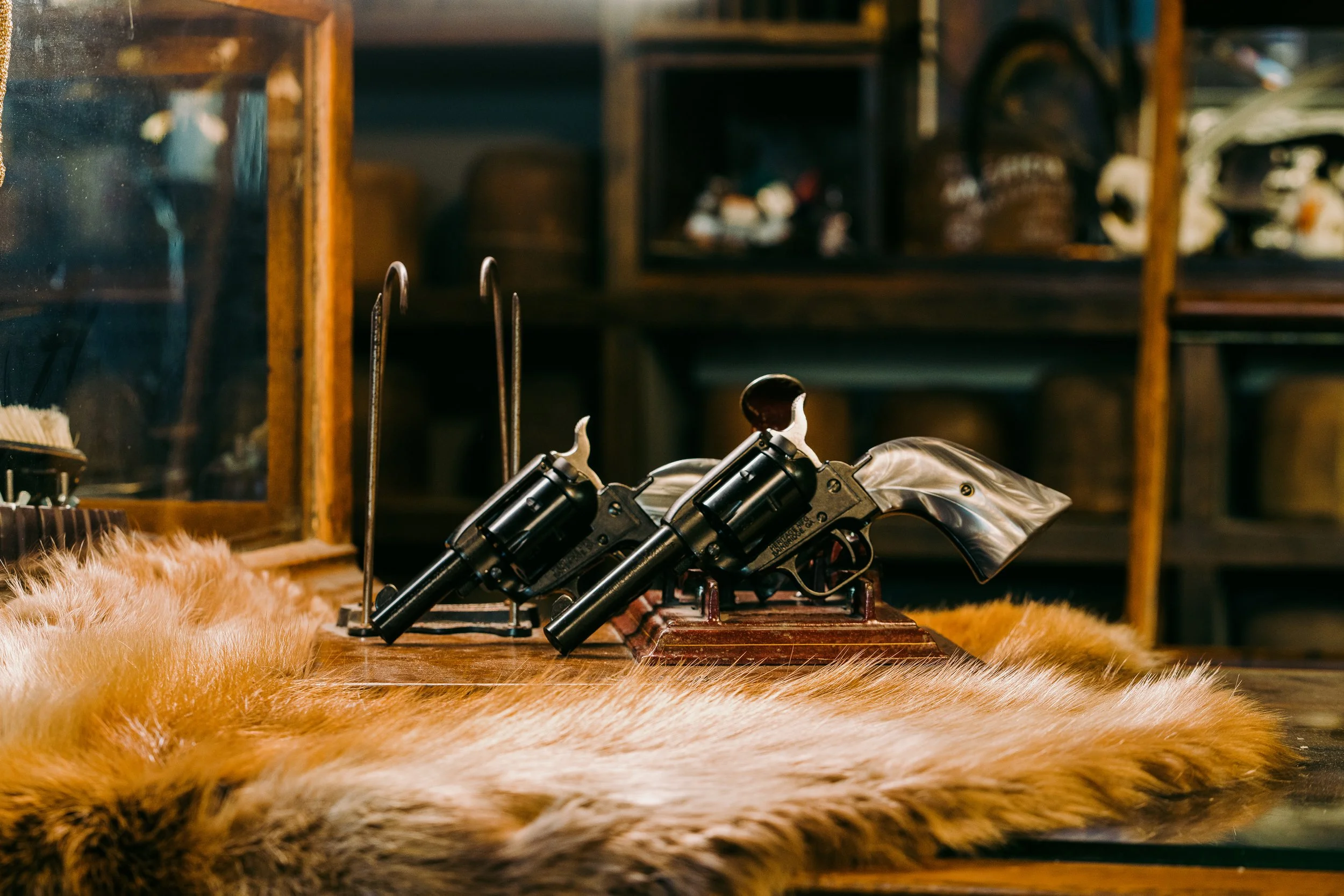 Two vintage revolvers with pearl grips displayed on wooden mounts, surrounded by animal fur in a rustic setting.