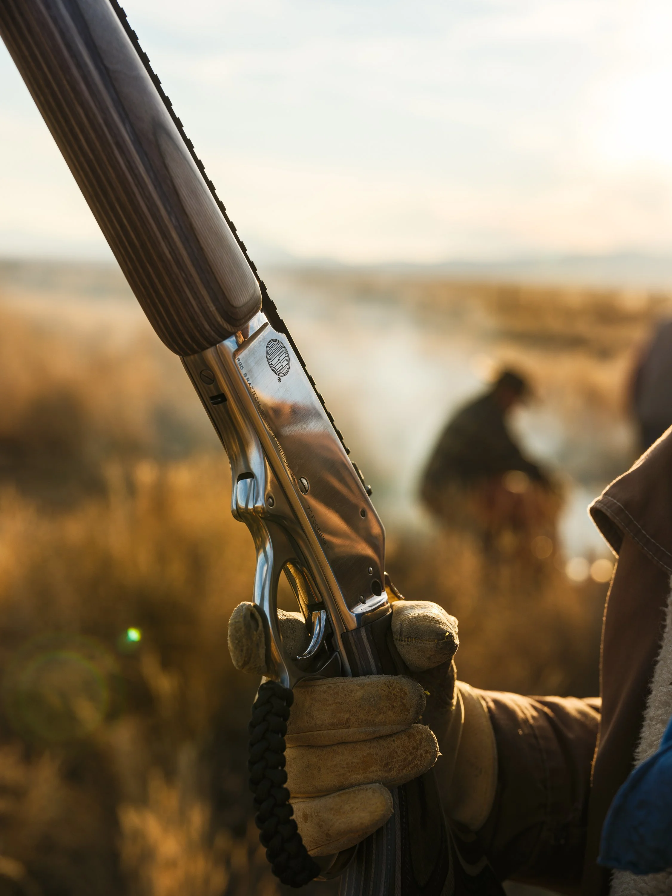 Close-up of a person holding a double-barreled shotgun with gloved hands in an outdoor setting.