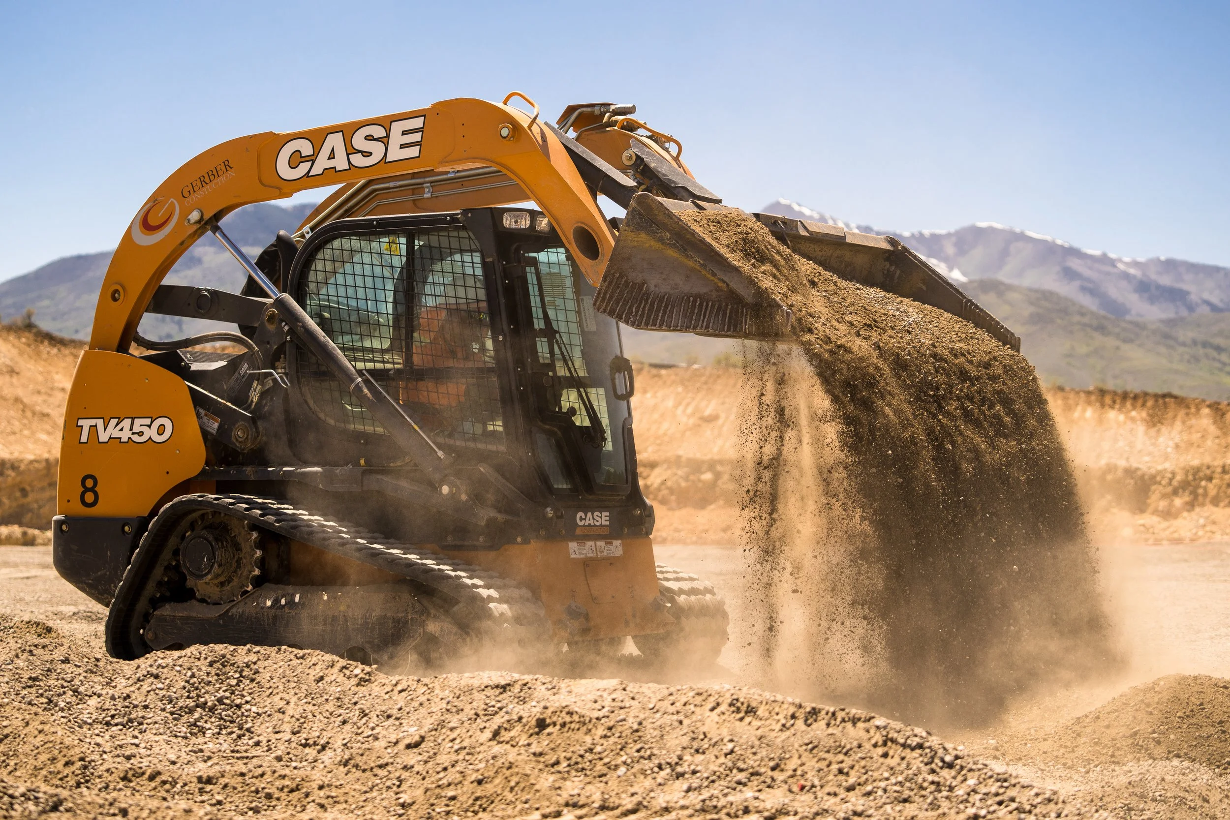 Skid steer loader moving dirt at a construction site with mountains in the background.