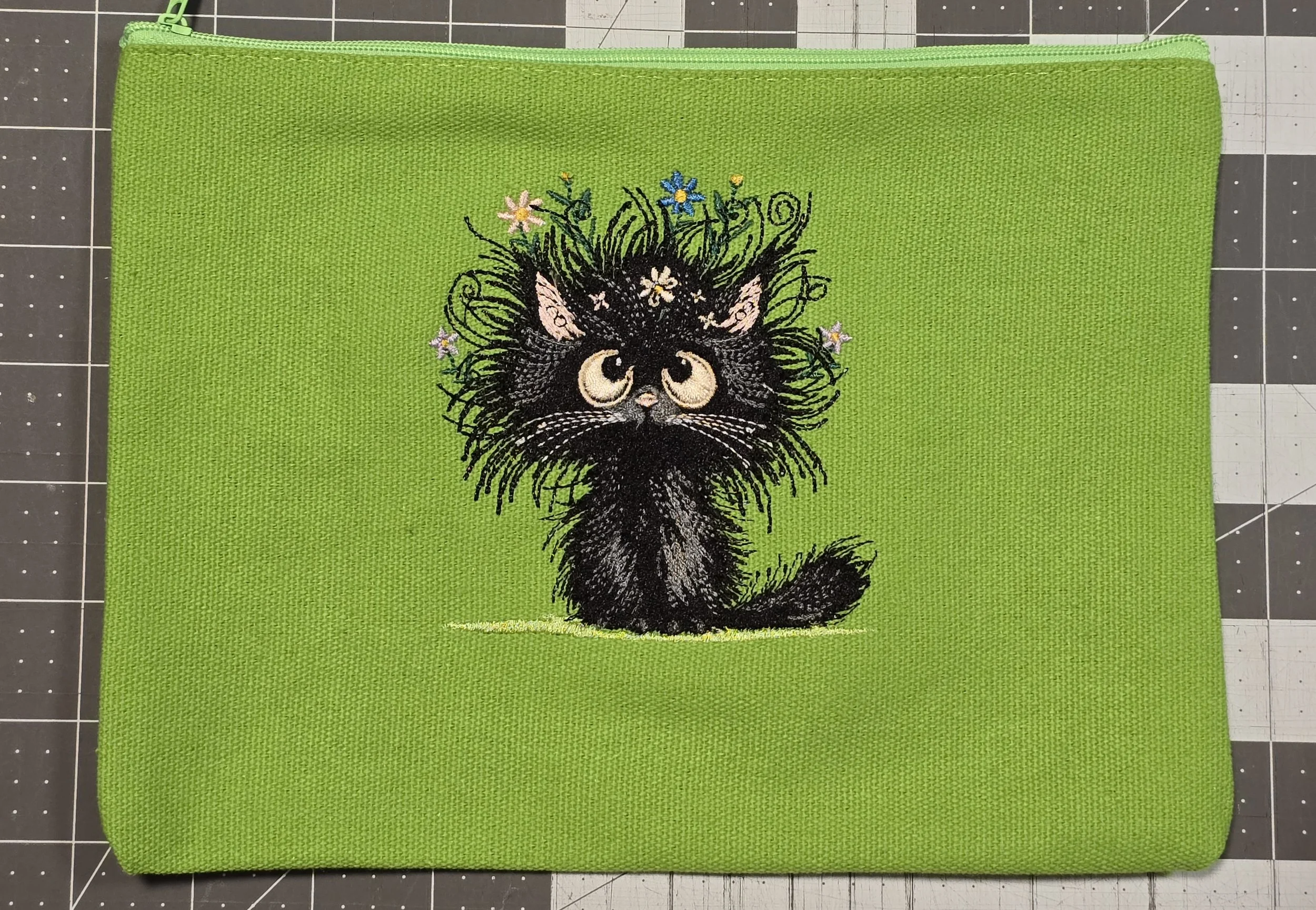 Green fabric pouch with embroidered black kitten with flowers and grass