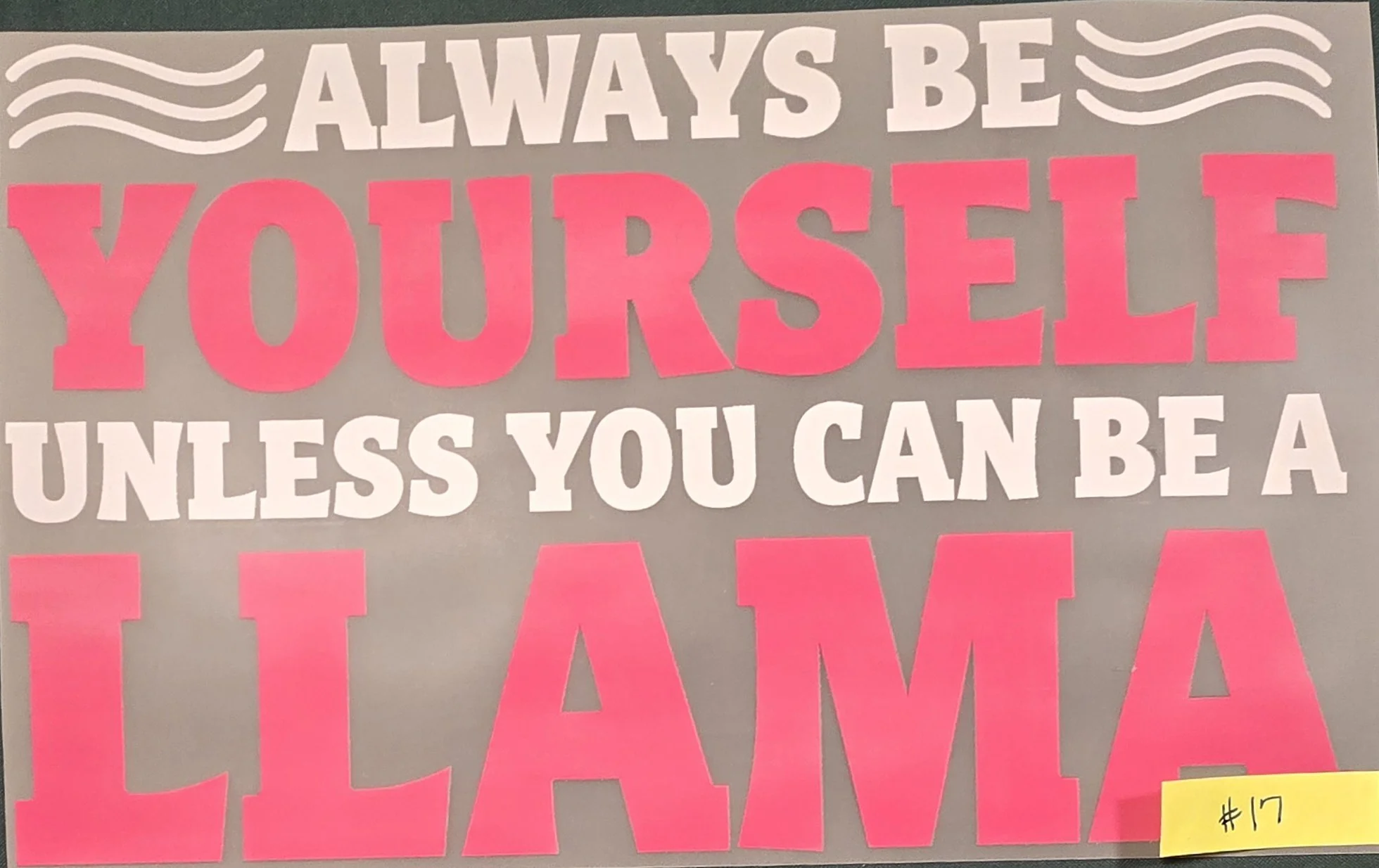A motivational poster with the quote, "Always be yourself unless you can be a [illegible]," in bold, colorful letters, with decorative wavy lines at the top and a yellow sticky note with the number 17 at the bottom right corner.