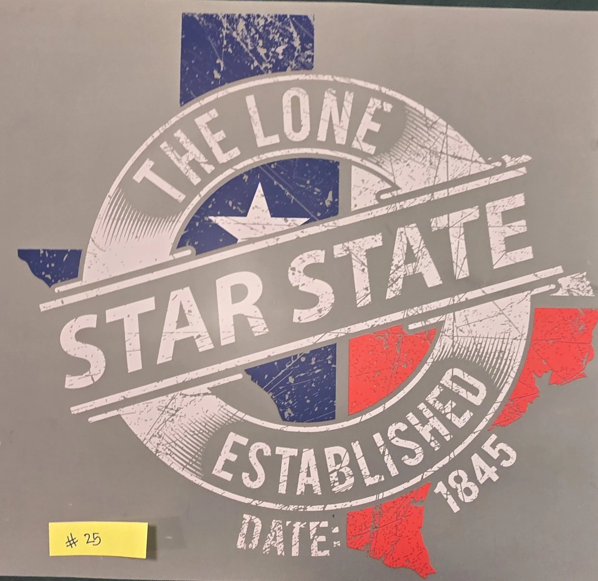 A printed sign with a circular design featuring the text 'The Lone Star State' and an outline of the state of Texas in red. The sign has a distressed, vintage look with a star in the design and some decorative lines. A yellow sticky note at the botto