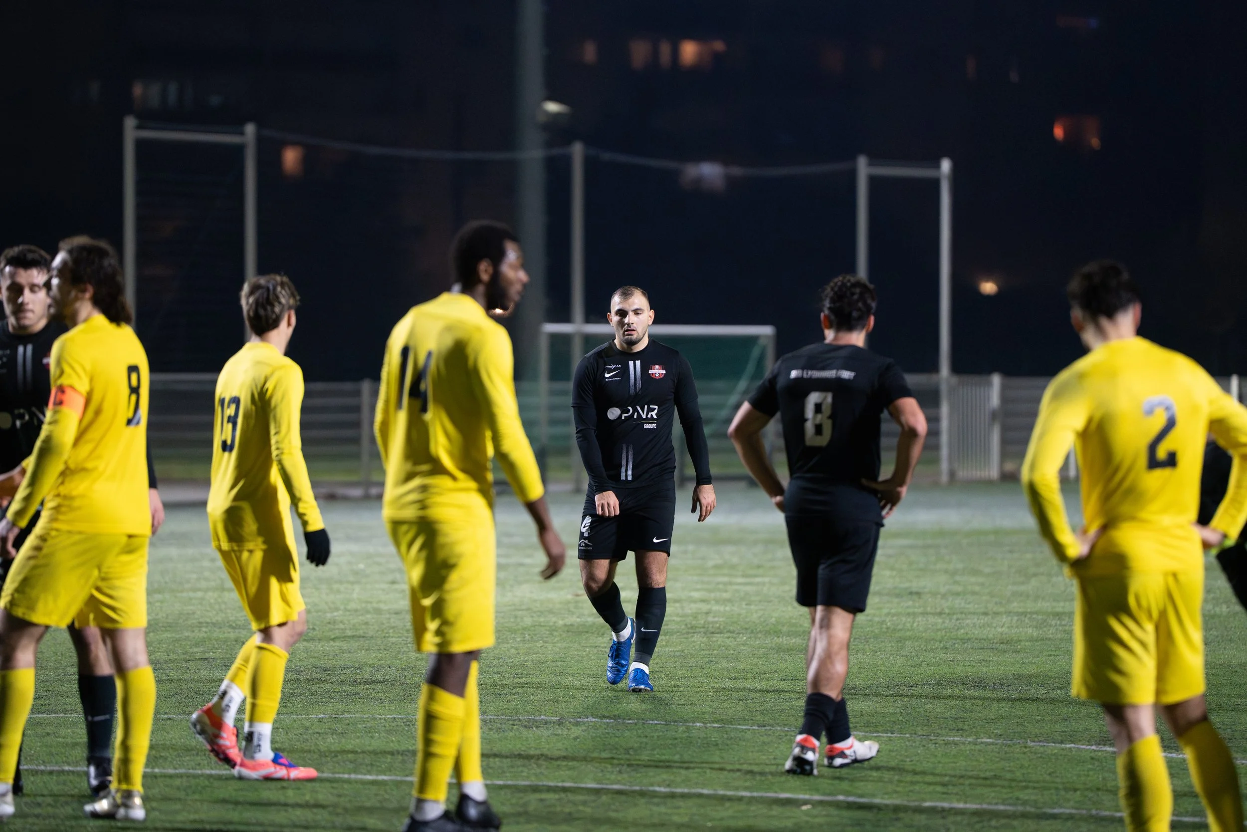 Une équipe de football en noir et jaune sur le terrain lors d'un match nocturne.