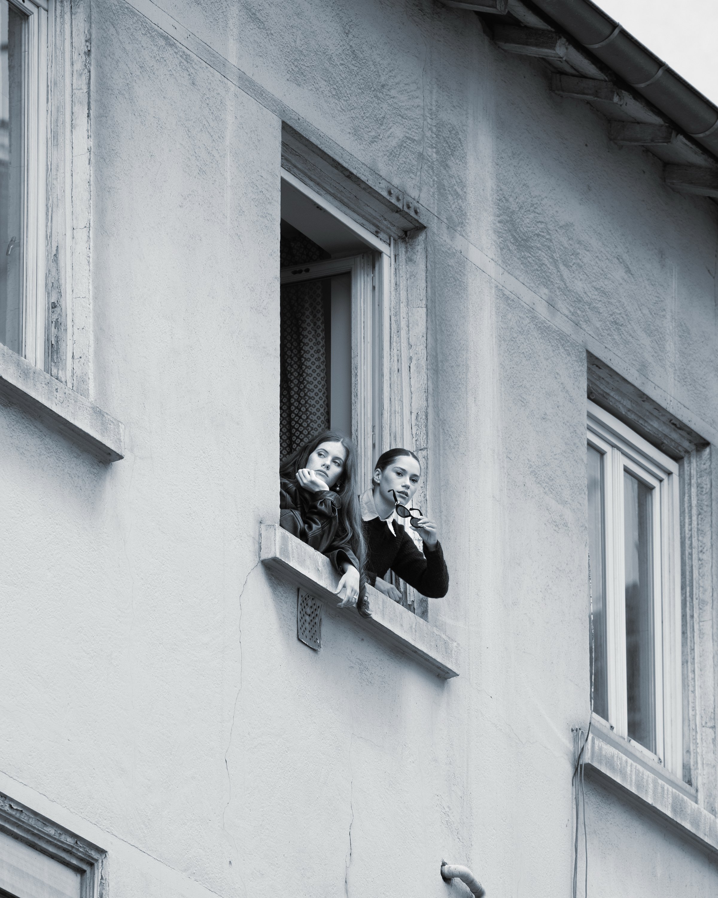 Deux femmes regardent par une fenêtre d'un immeuble en béton, l'une tenant des lunettes.