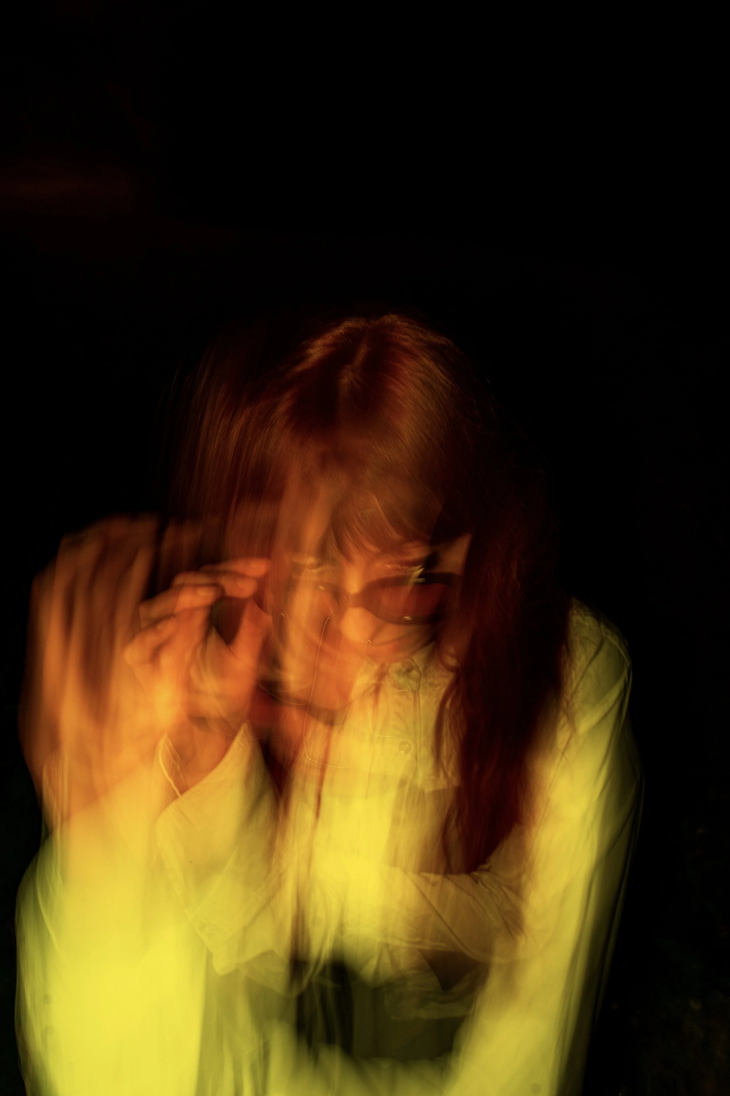 Une femme portant des lunettes et une veste jaune, photo floue avec mouvement, fond noir.
