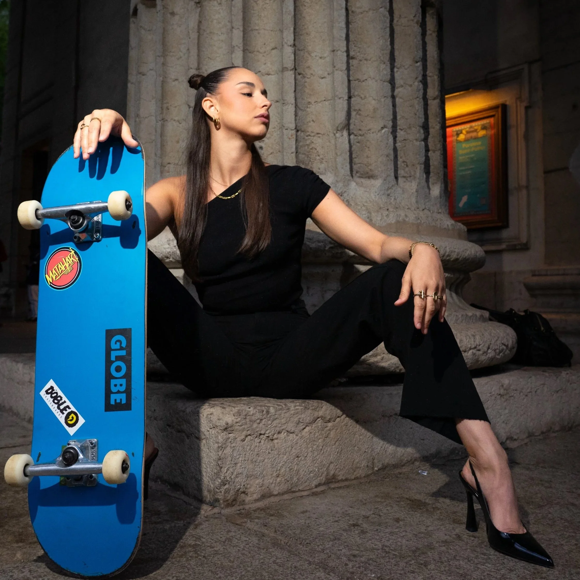 Charlotte Cury assise en talons aiguilles avec un skateboard, shooting éditorial urbain à Lyon.