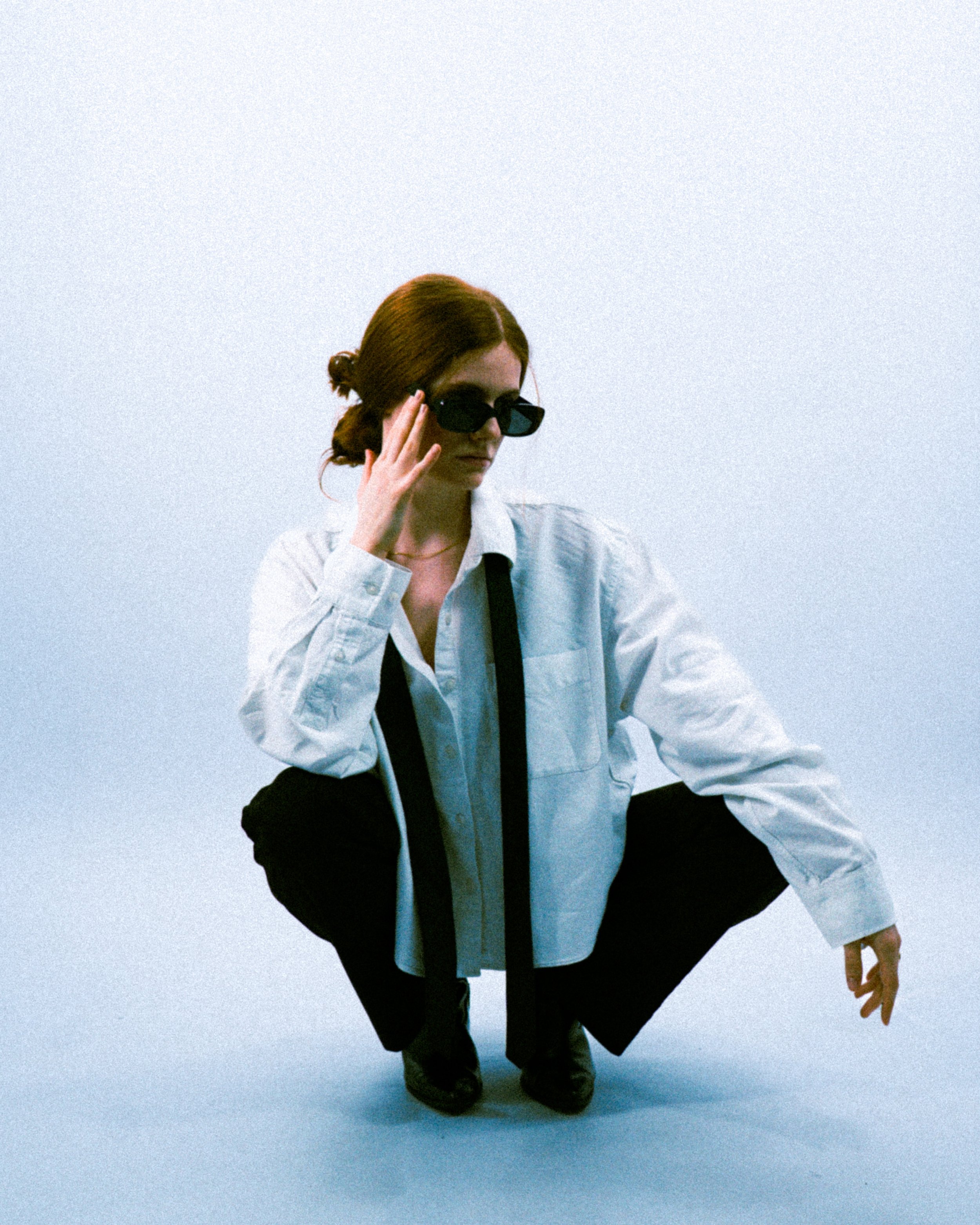 Portrait féminin accroupi regard direct, shooting éditorial studio minimaliste.