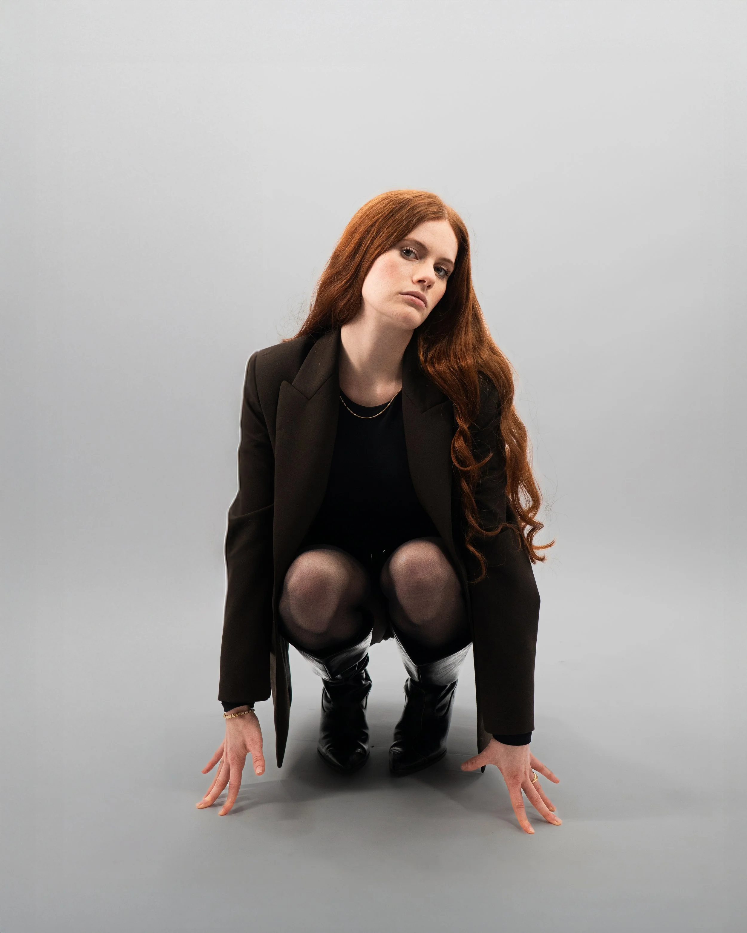 Femme accroupie en studio regard direct, photographie éditoriale moderne.