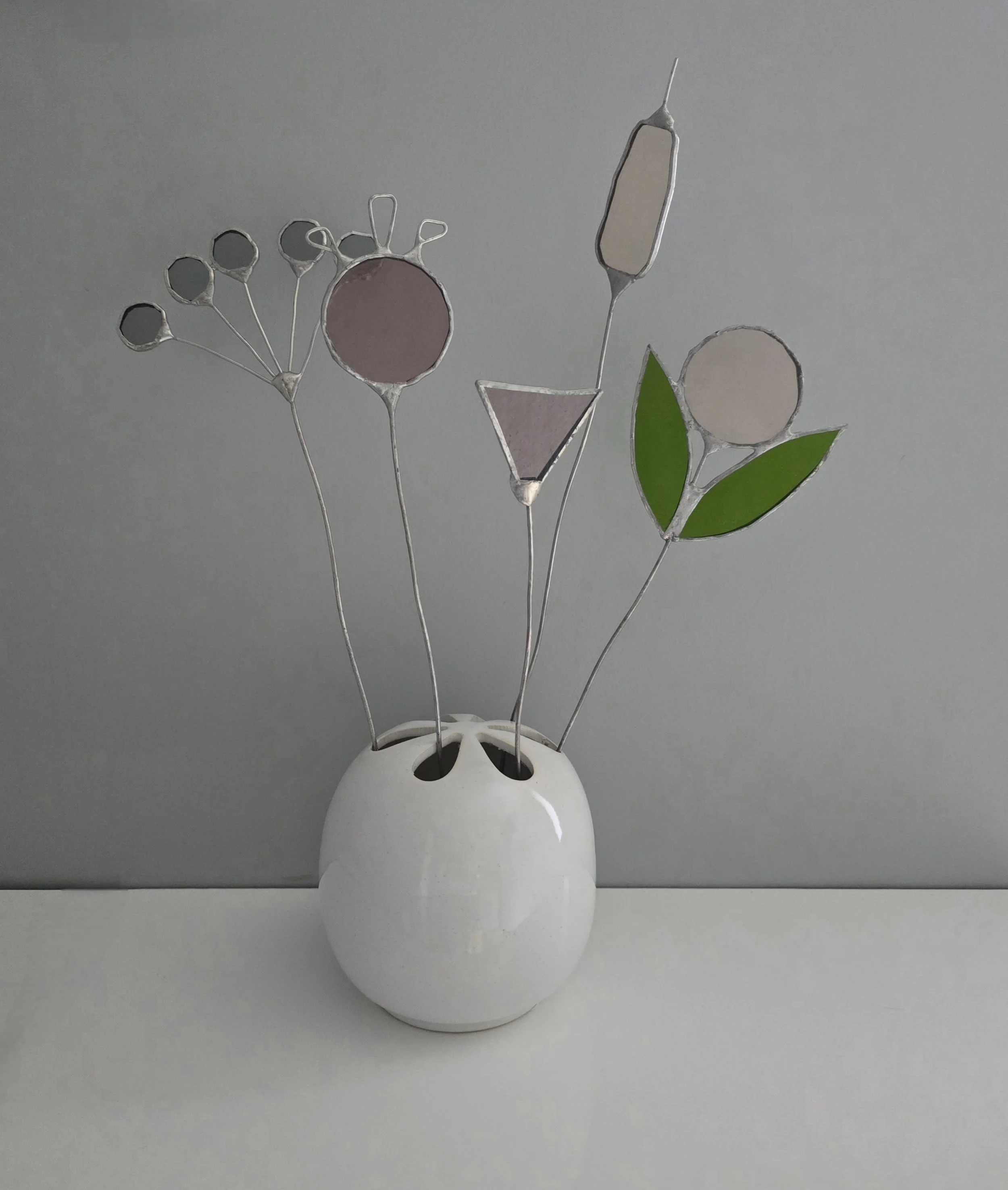 Stained glass sculpture with floral designs on a natural wood base against a brick wall background.