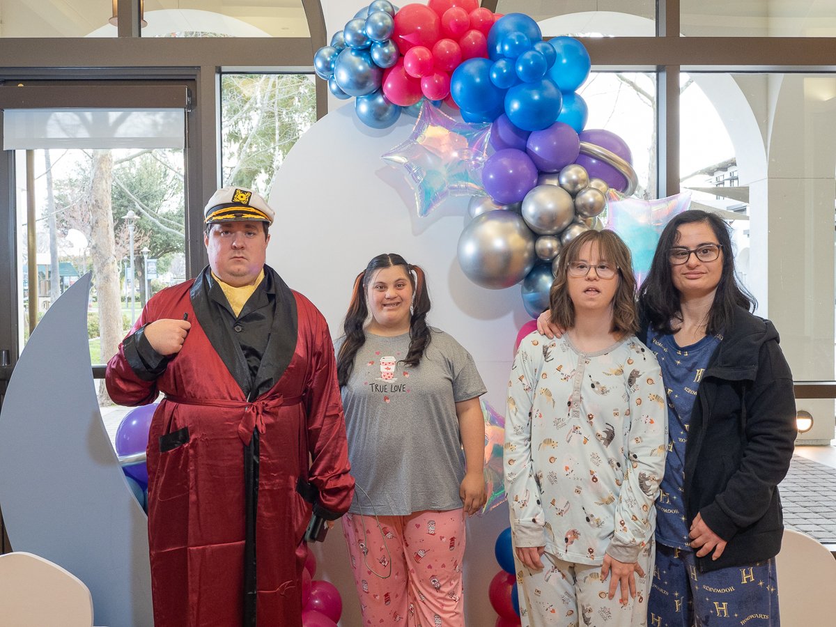 Group of four people in pajamas standing in front of a balloon arch indoors.