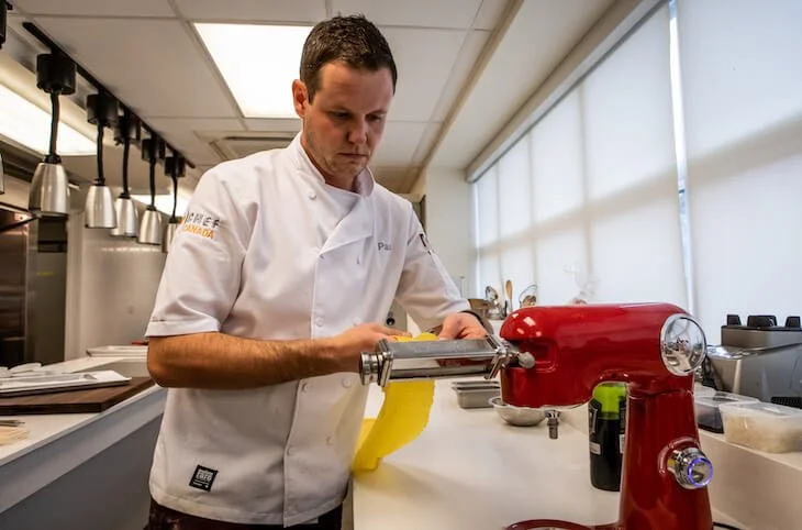 Chef in white coat making pasta on red machine