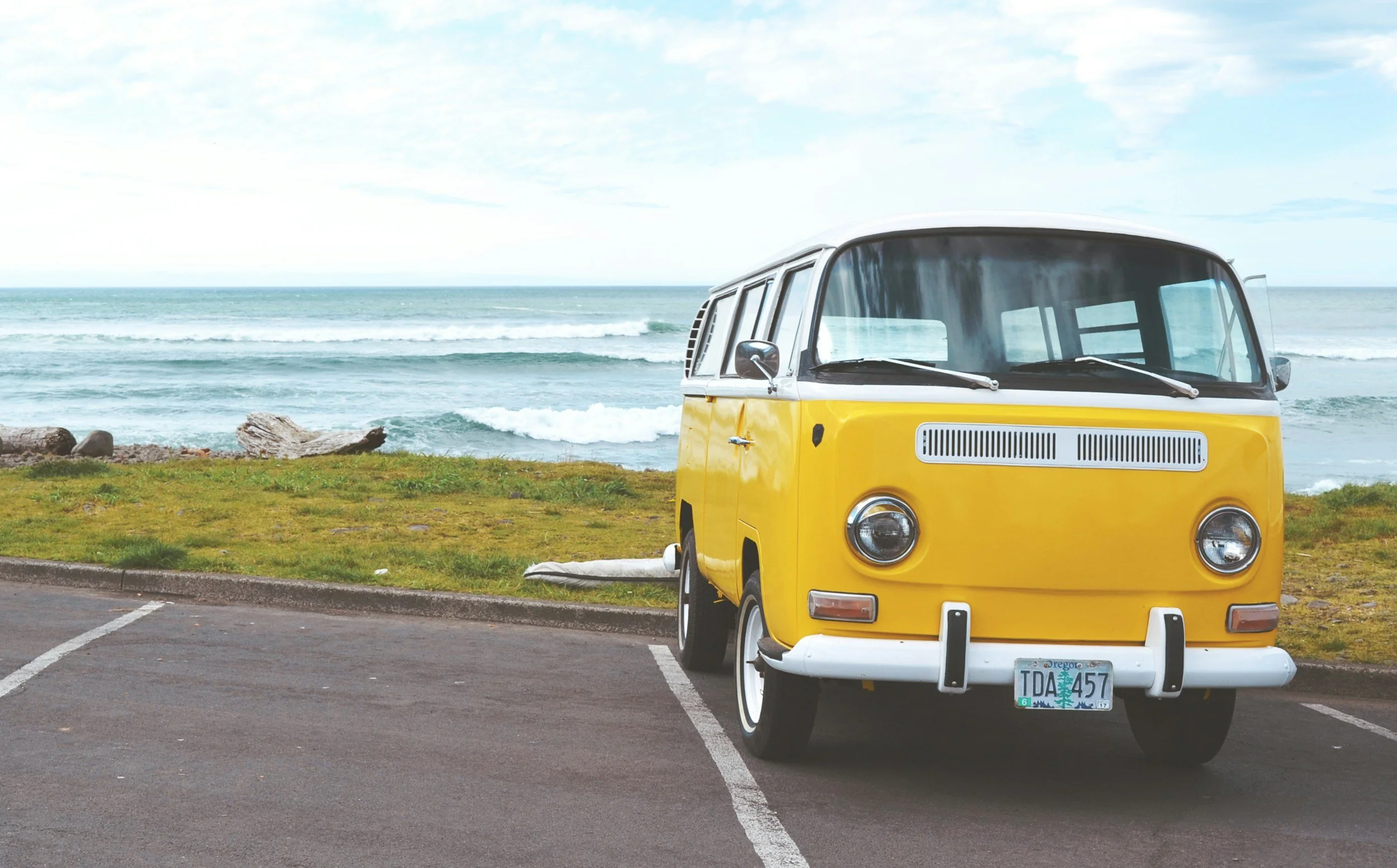 Yellow vintage Volkswagen van parked near the ocean with waves and cloudy sky in the background