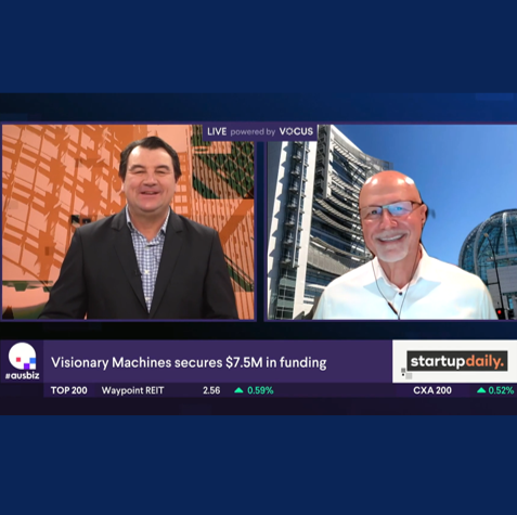 Two men are on a video call, with a news banner about major funding for Visionary Machines and stock market updates at the bottom.
