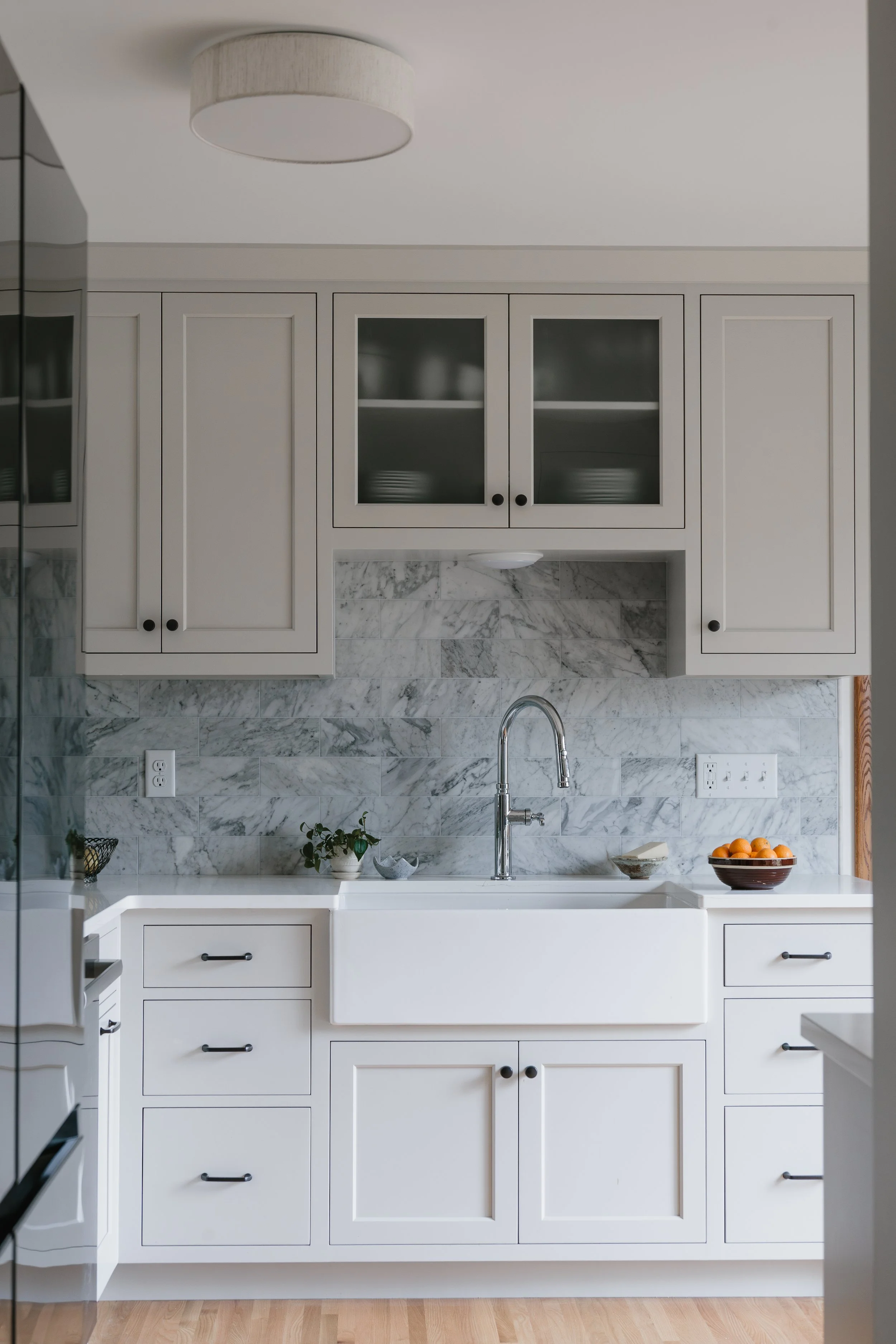 Historic kitchen renovation with white cabinets, marble backsplash, and farmhouse sink in Minneapolis