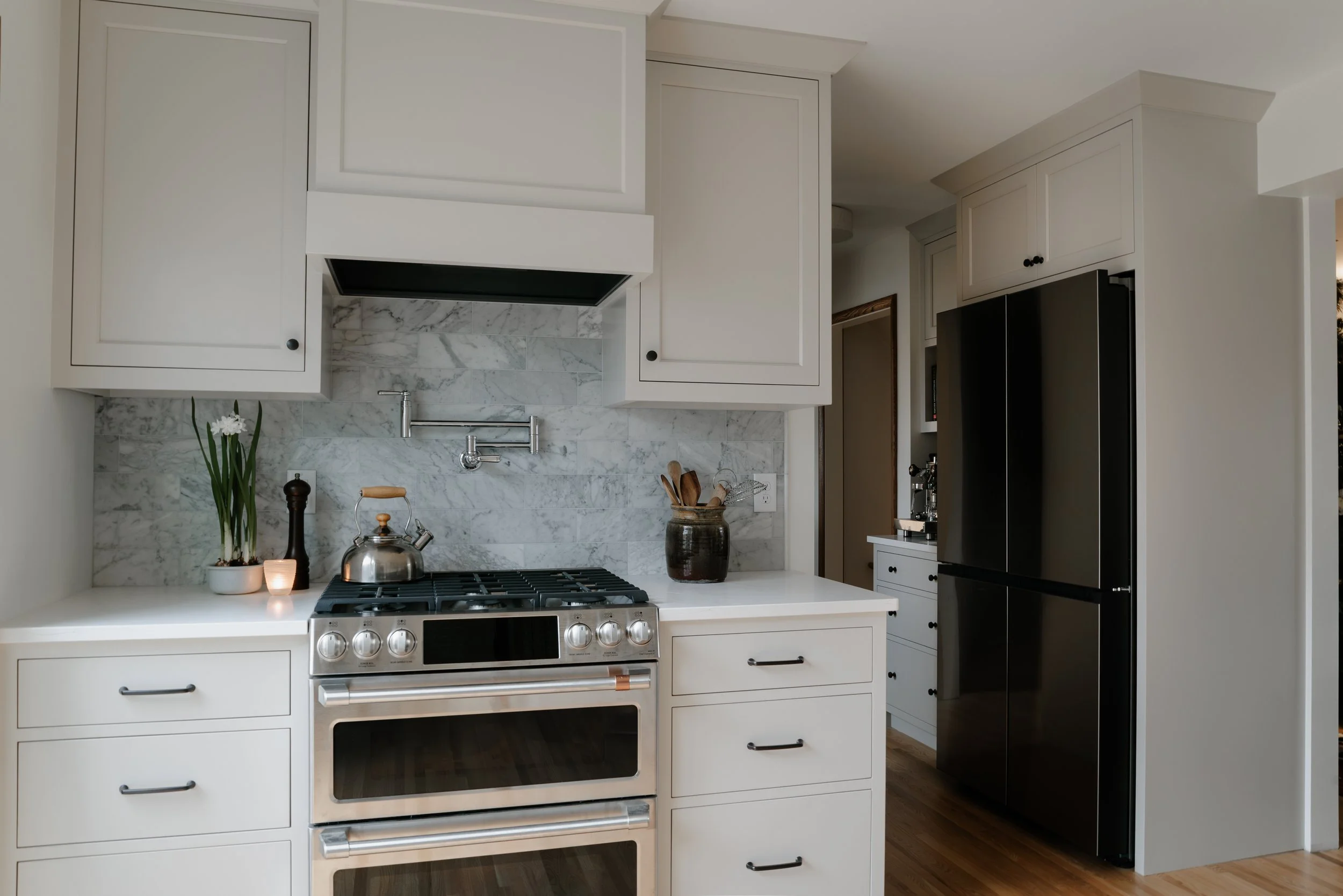 White kitchen renovation with gas range, marble backsplash, and stainless appliances in Minneapolis