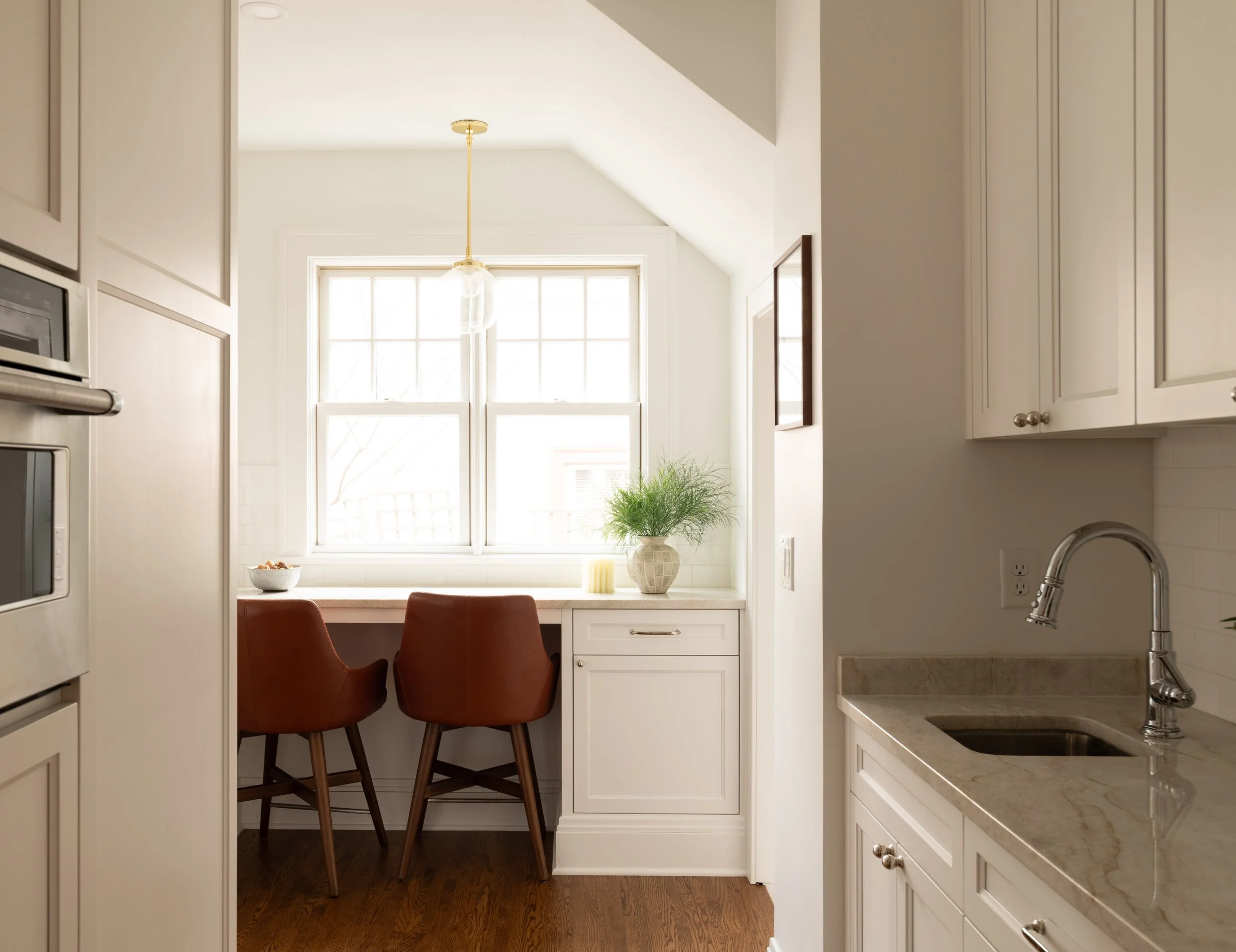 Bright kitchen renovation company in Minnesota. This image looks through a kitchen to a breakfast nook overlooking a window. The cabinetry is white, bright, and high quality, while a neutral countertop and backsplash indicate a peaceful, clean home.