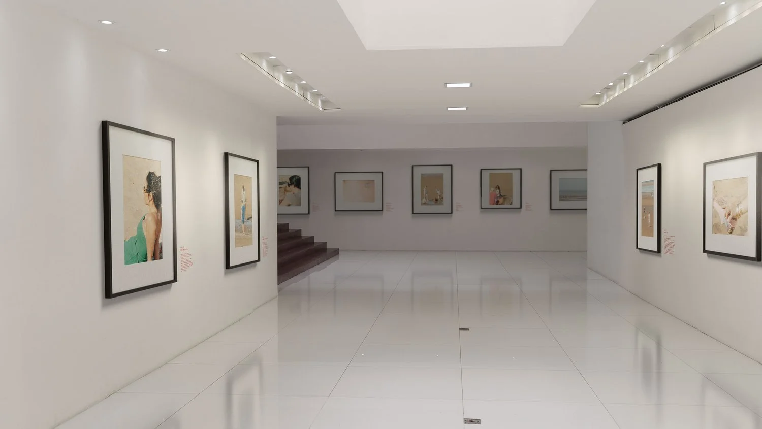 Contemporary art gallery with framed paintings on white walls, polished white floors, and ceiling lights illuminating the artworks.