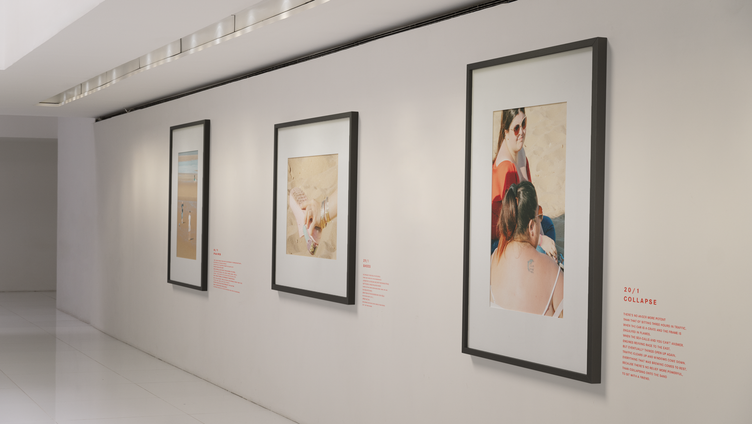 An art gallery with framed photographs of people at the beach hung on a white wall.