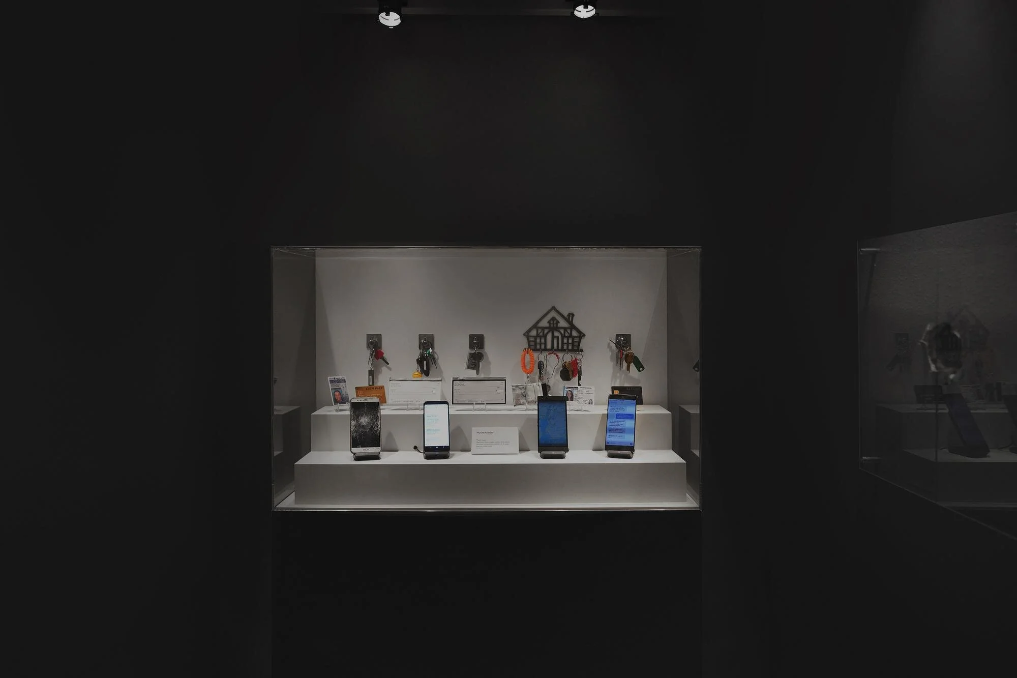 Display case with smartphones and keychains in a museum or store setting.