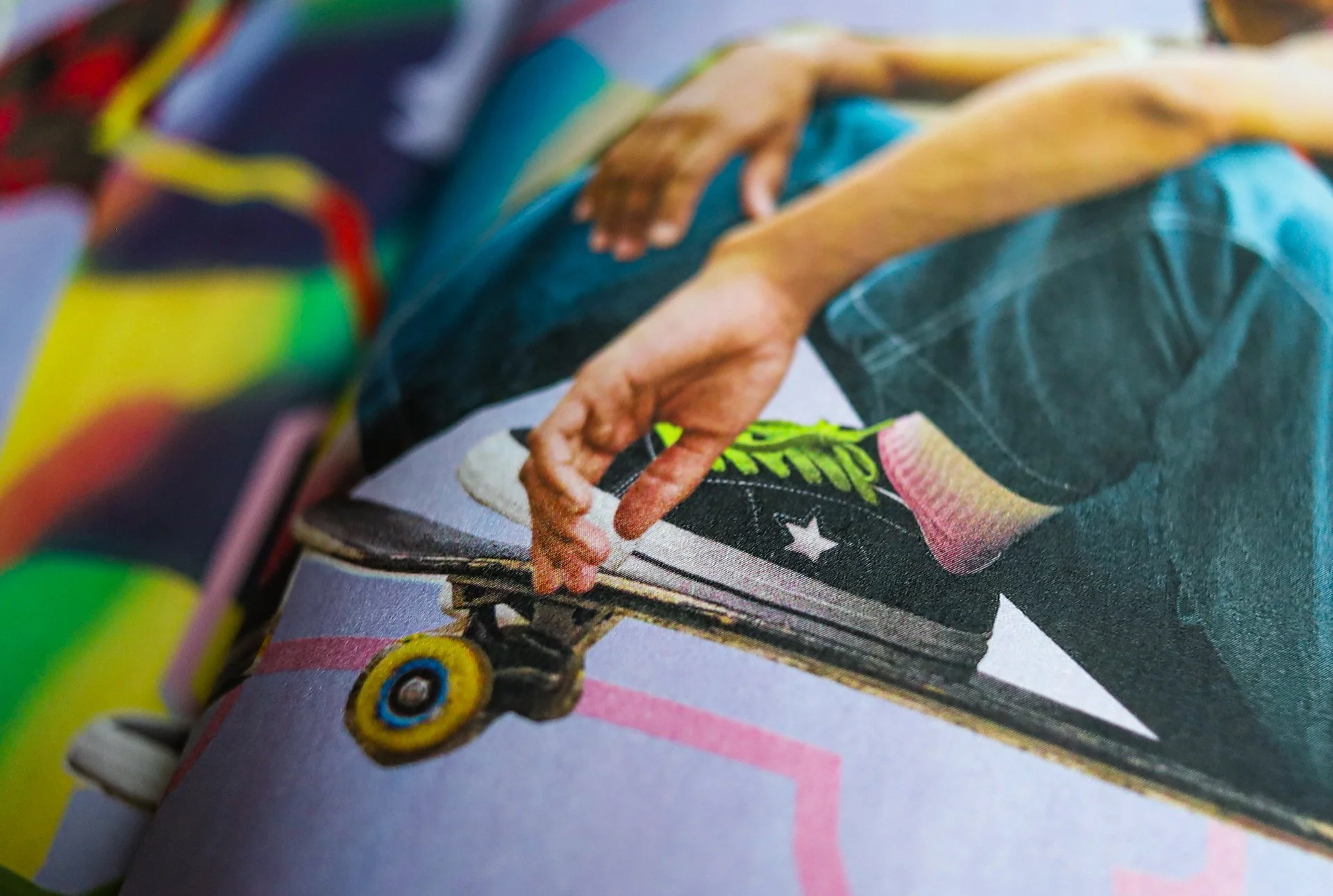 Close-up of a person’s hand adjusting a skateboard wheel with a colorful design, wearing a dark denim overall and bright socks.