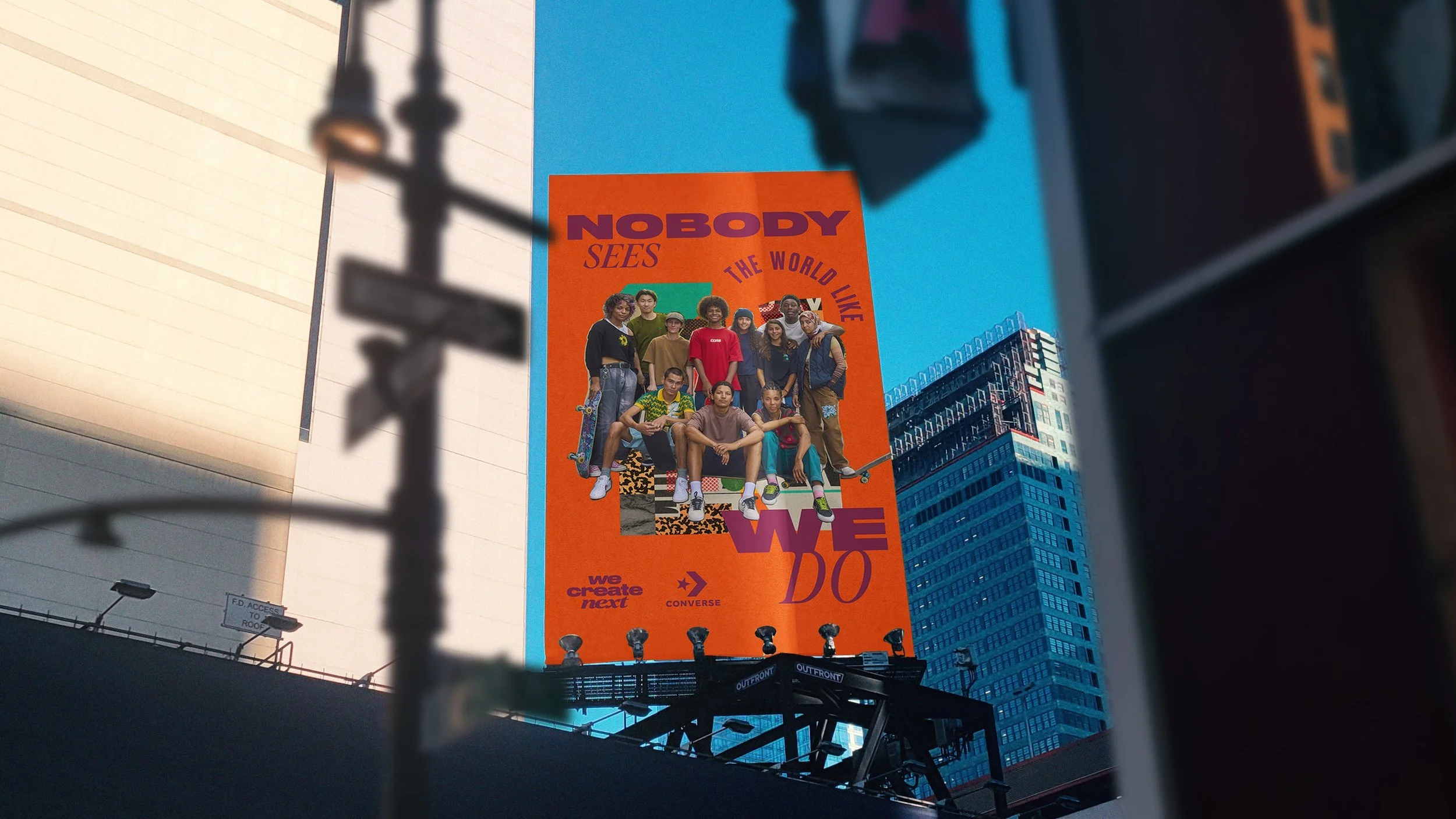 A large orange billboard displaying a diverse group of young people, with text that reads "NOBODY SEES THE WORLD LIKE WE DO" and smaller text "we create next" and "CONVERSE." The billboard is seen against a blue sky in an urban setting with tall buildings.