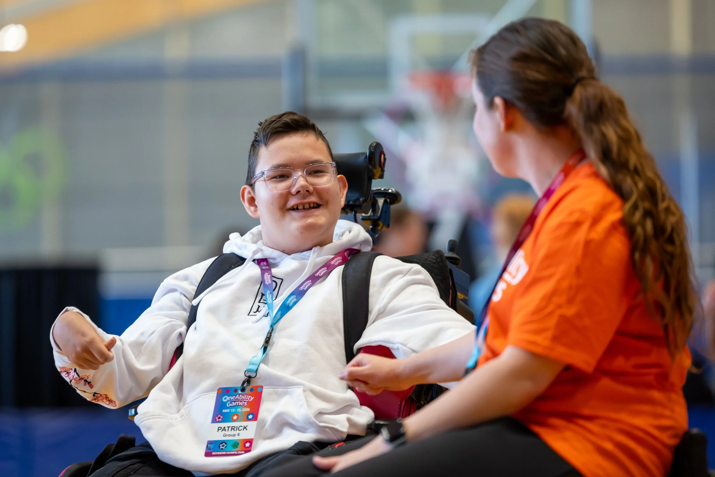 A young boy in a power wheelchair smiles at a volunteer