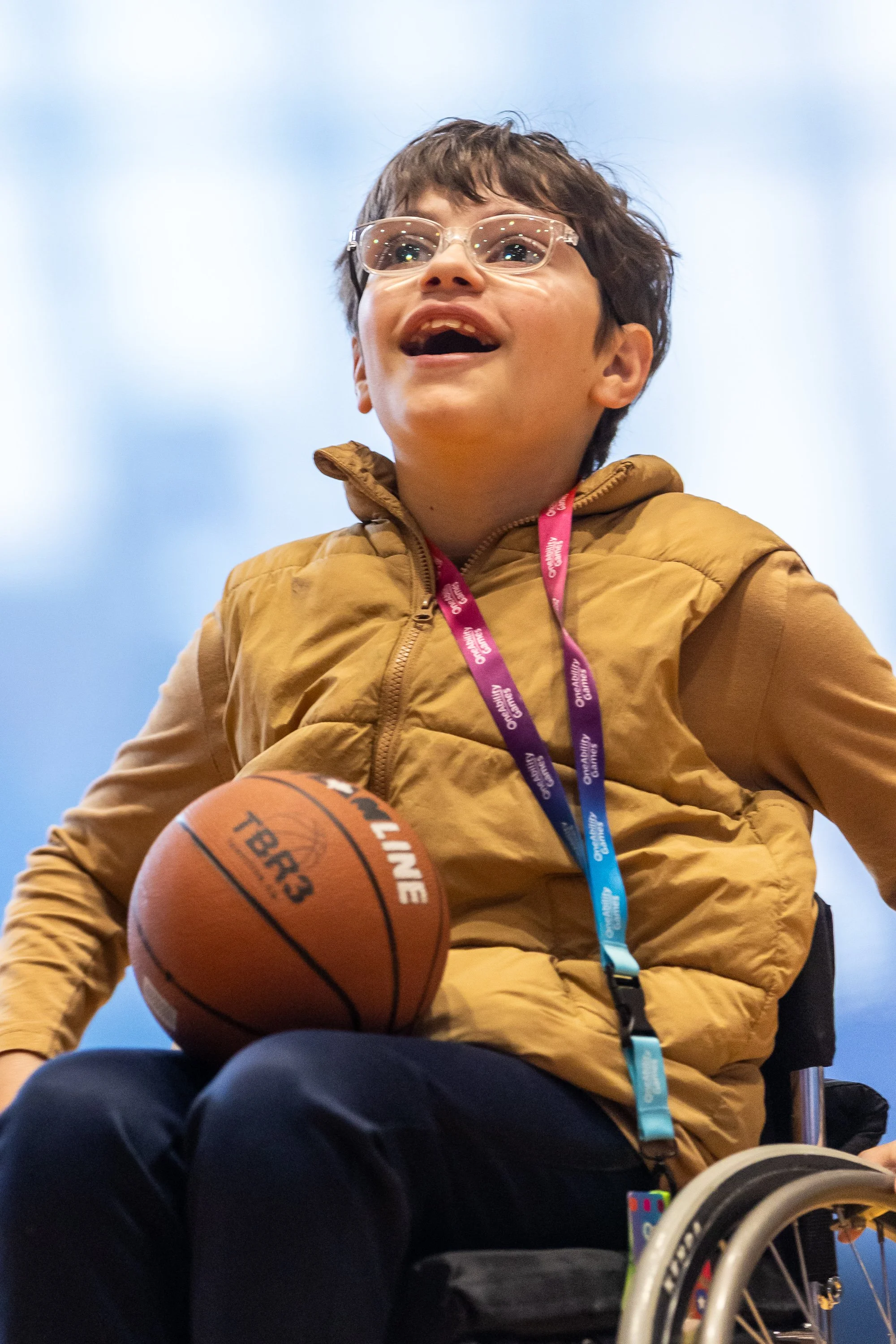 Elementary school boy wearing glasses sits in a sport wheelchair with a basketball on his lap