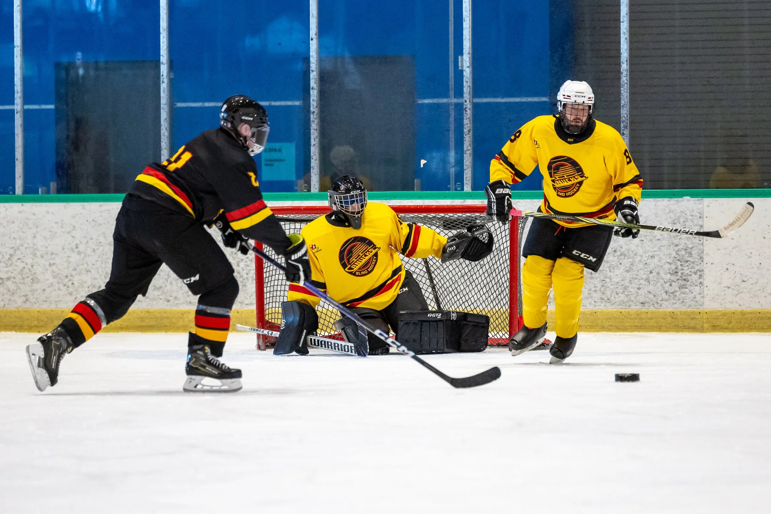 Two blind hockey players skate towards the net to take a shot