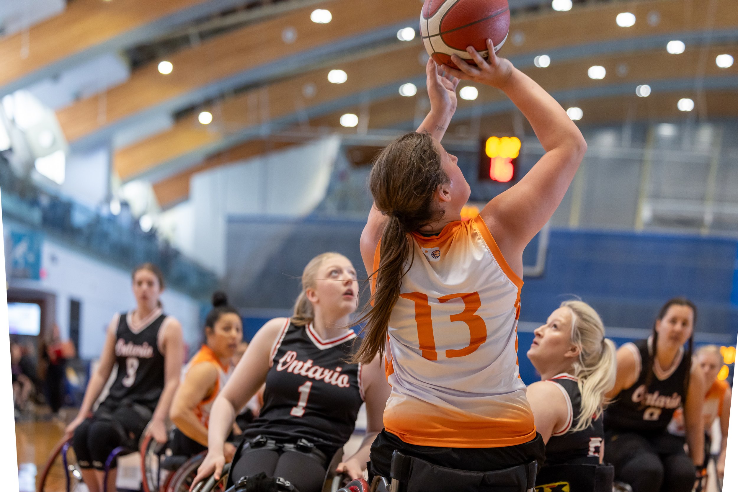 A female BC Wheelchair Basketball athlete, wearing an orange jersey, goes to make a shot