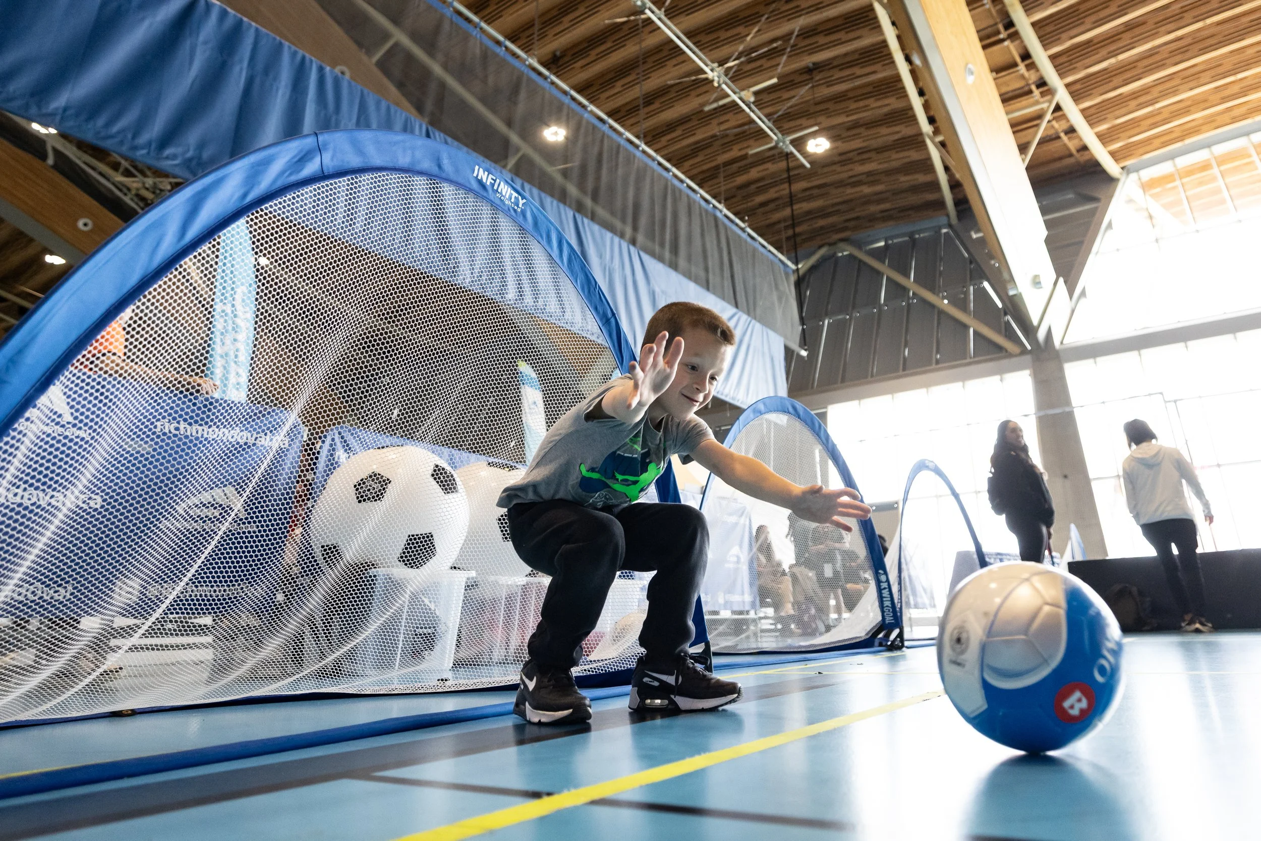 A young boy crouches in front of a soccer net, ready stop the incoming soccer ball