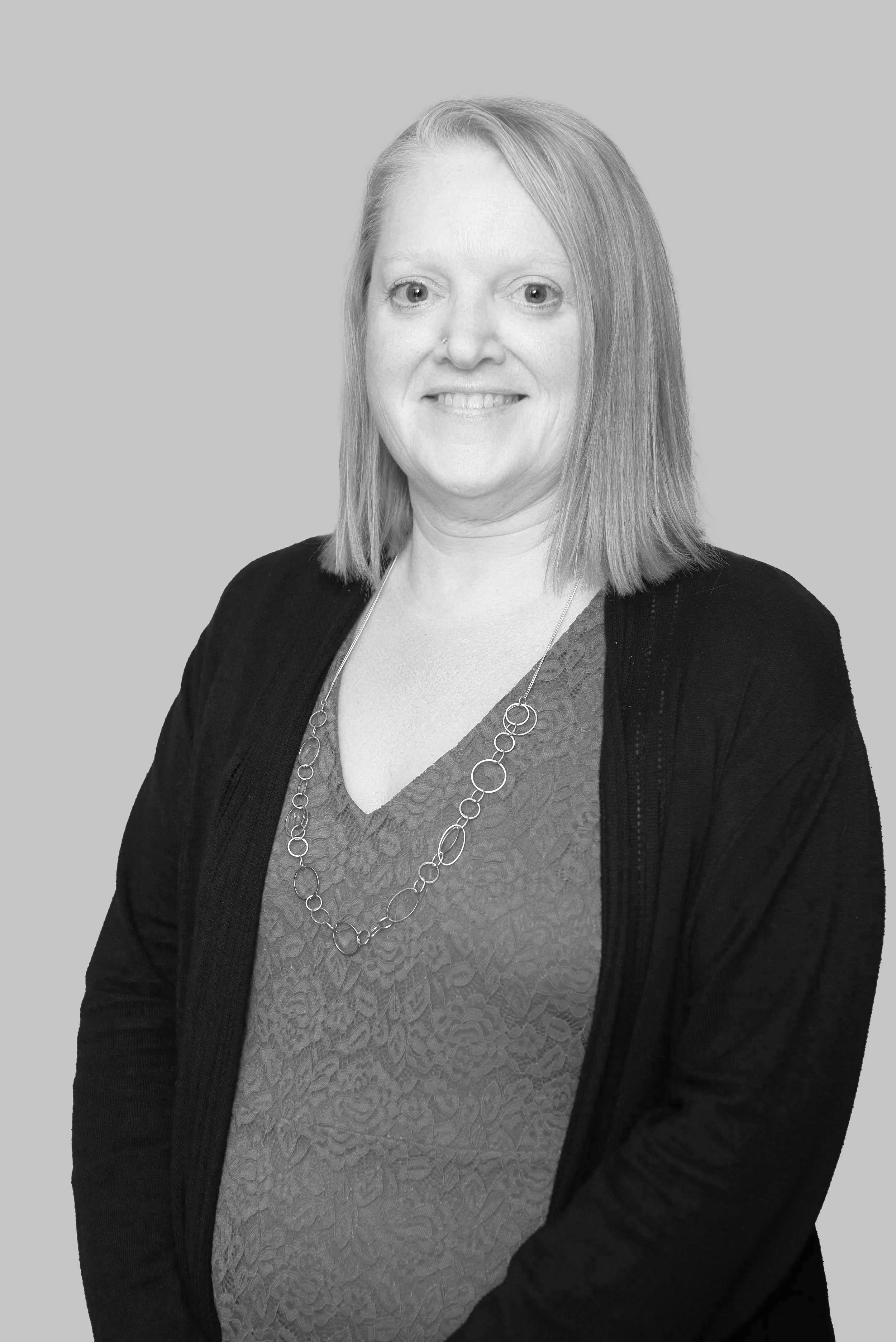 Jenn is a white woman with shoulder length straight blonde hair and blue eyes. She is wearing a textured red V neck, black cardigan, and long chain necklace.