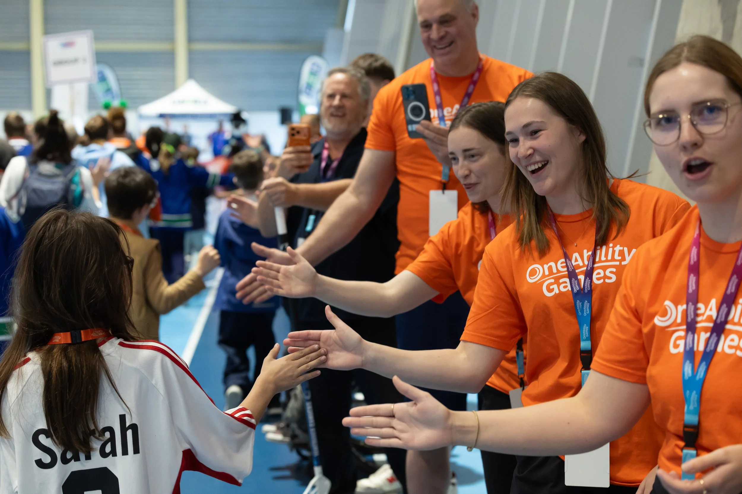 A line of smiling volunteers in orange shirts high five students as they parade in